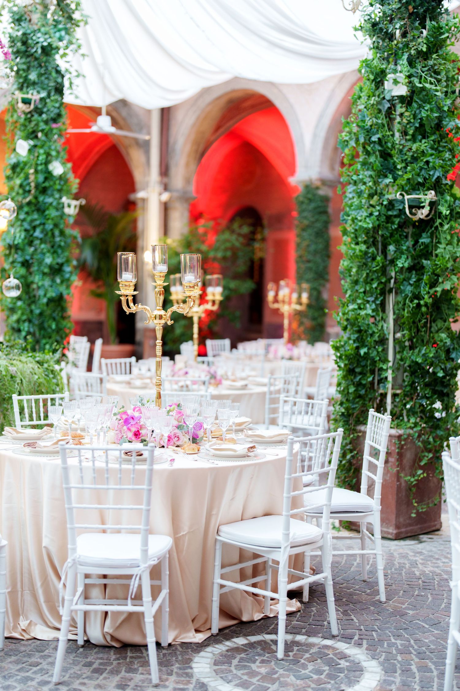 White Chiavari chairs and round tables set for wedding reception with greenery and red accents.