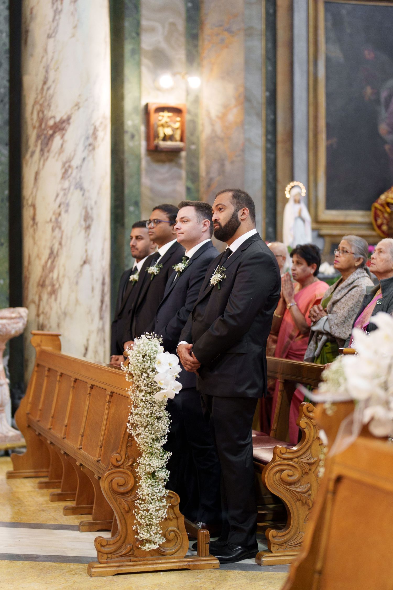 Wedding guests seated in wooden church pews decorated with baby's breath floral arrangements.