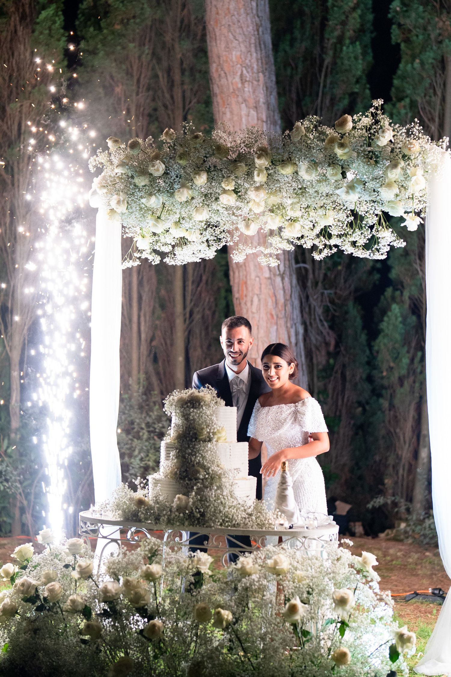 A romantic wedding scene with fairy lights and floral arrangements in a wooded setting.