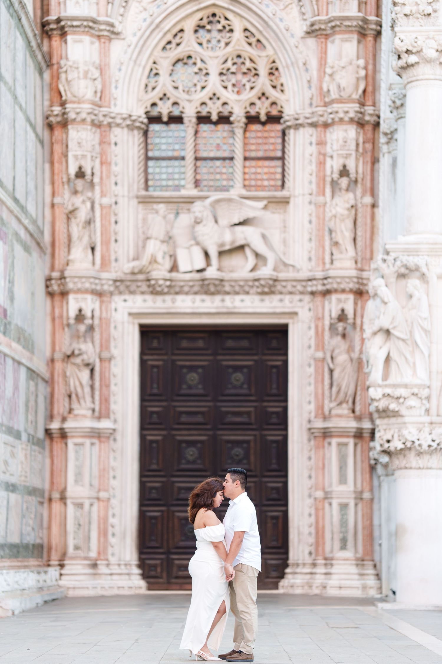 Romantic couple embraces in front of an ornate Italian cathedral with Gothic architecture and carved stone details.
