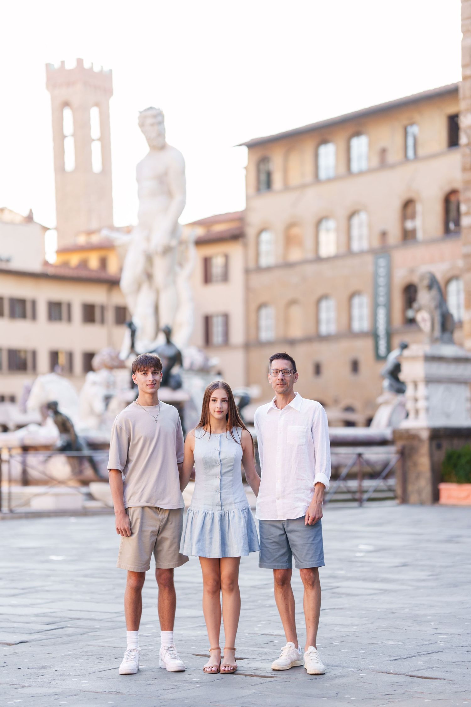Three people standing in a plaza in Florence, Italy with the historic Palazzo Vecchio and statues in the background.