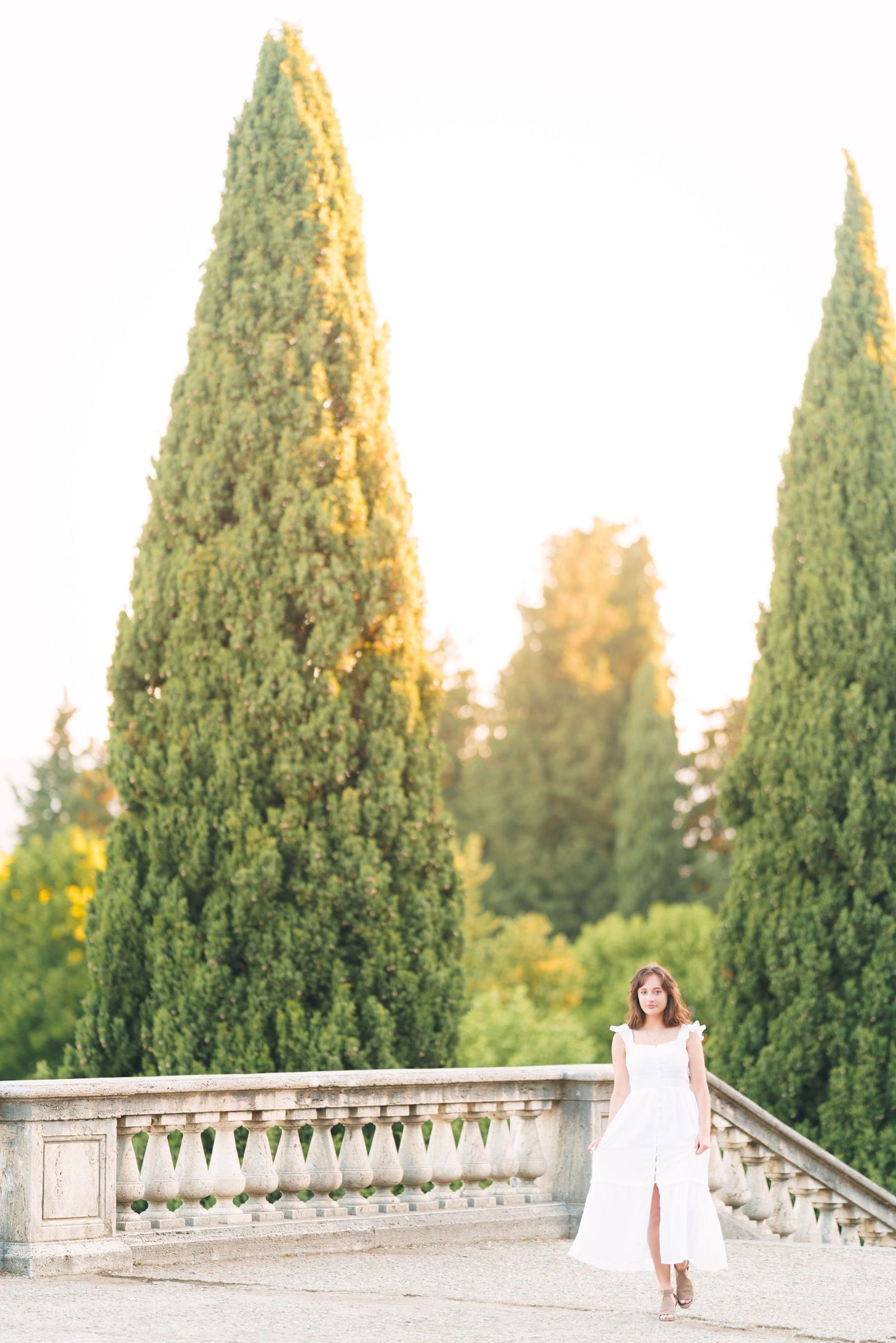 A scenic garden terrace with tall cypress trees and stone balustrade during golden hour.