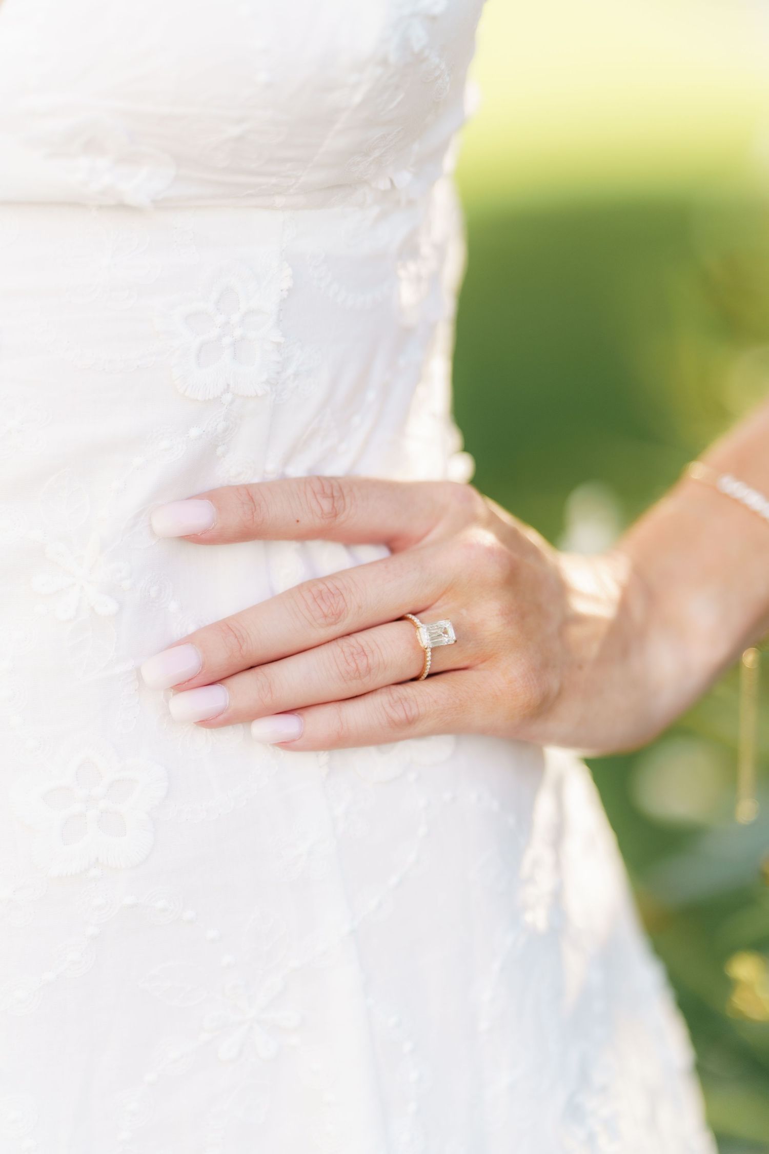 Close up of a bride's hand resting on her white wedding dress showing her engagement ring in soft natural light.
