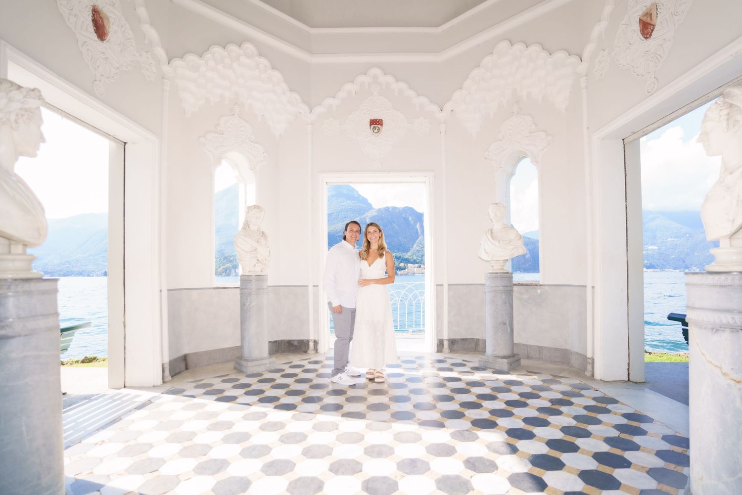 White interior room with a checkered floor pattern and arched windows overlooking a blue ocean view.