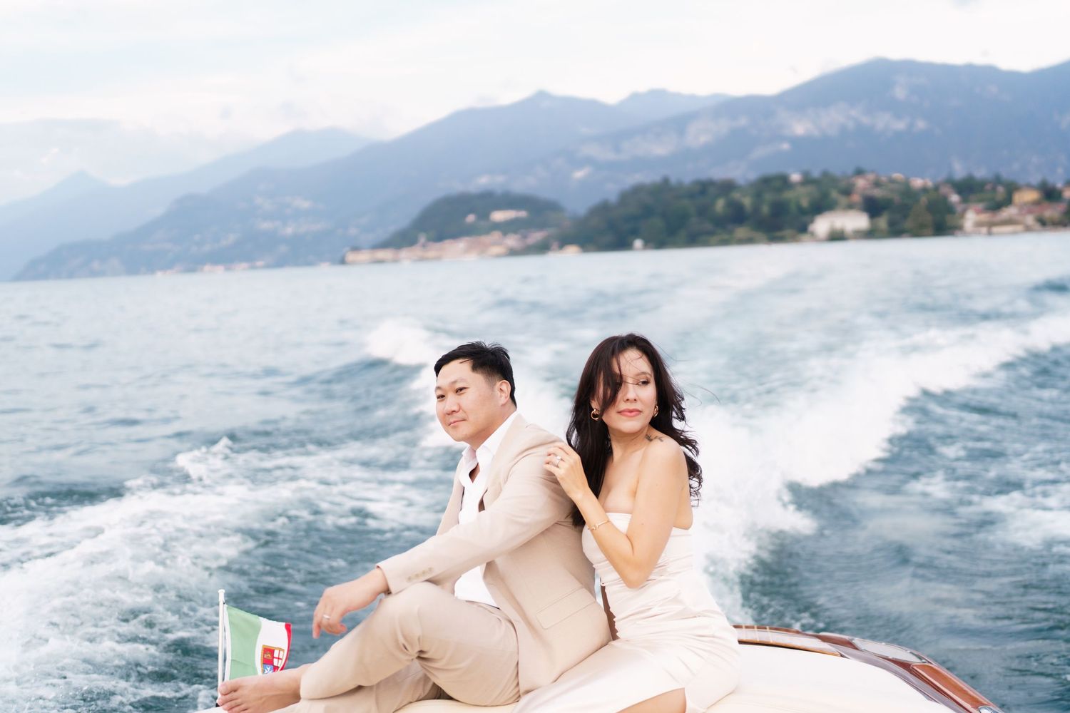 Couple enjoys romantic boat ride along scenic mountain coastline in white attire.