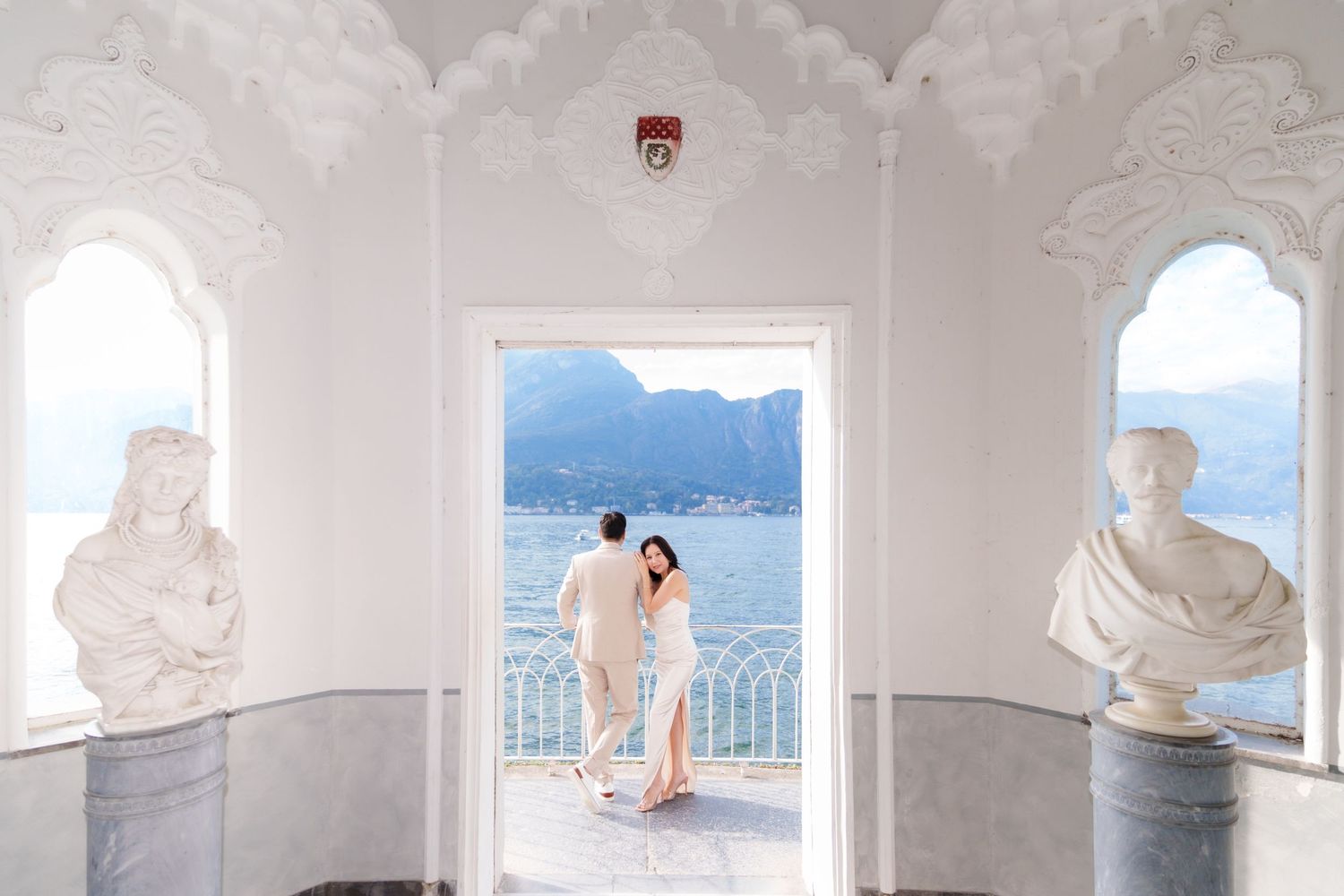 White arched hallway with ornate architectural details and a view of mountains and water through the windows.