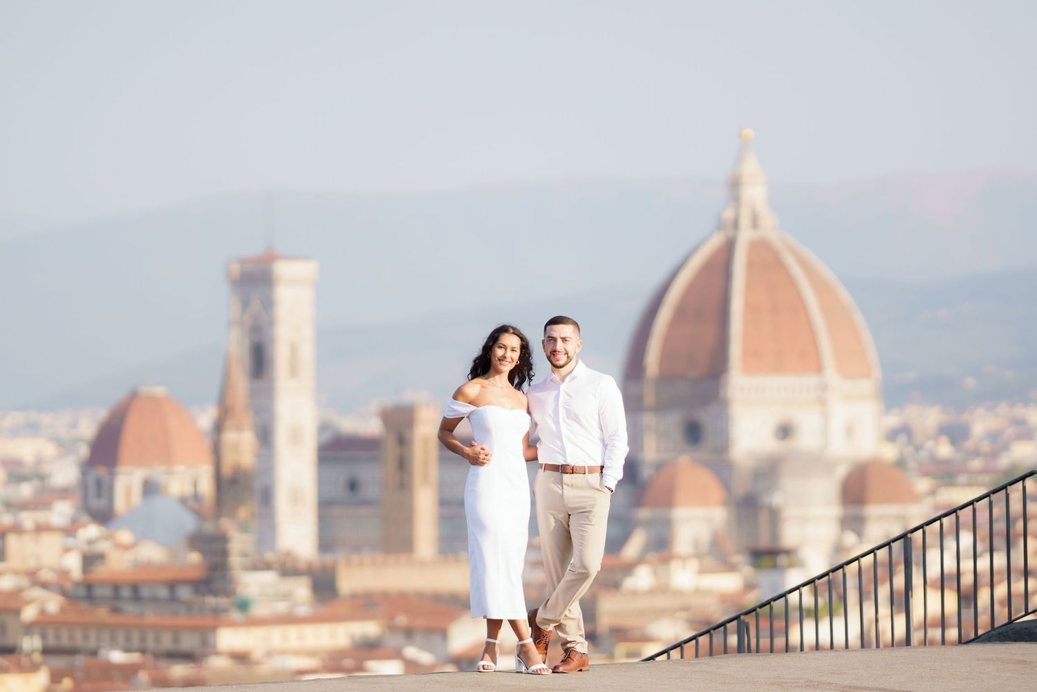 Romantic couple in white outfits pose against the iconic Florence skyline with Duomo cathedral visible in background.