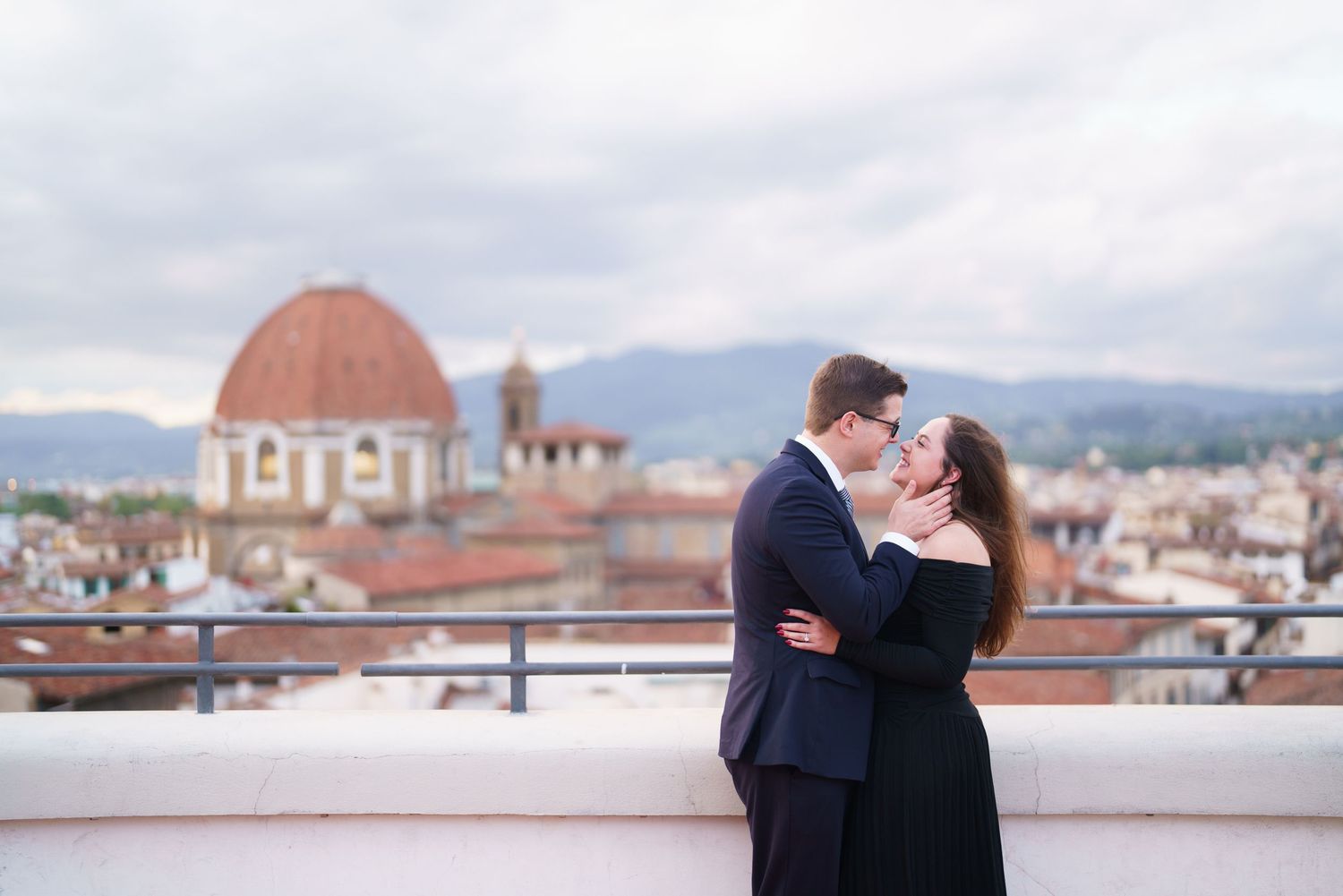 A romantic couple embraces on a rooftop terrace overlooking Florence with the Duomo cathedral dome in the background.