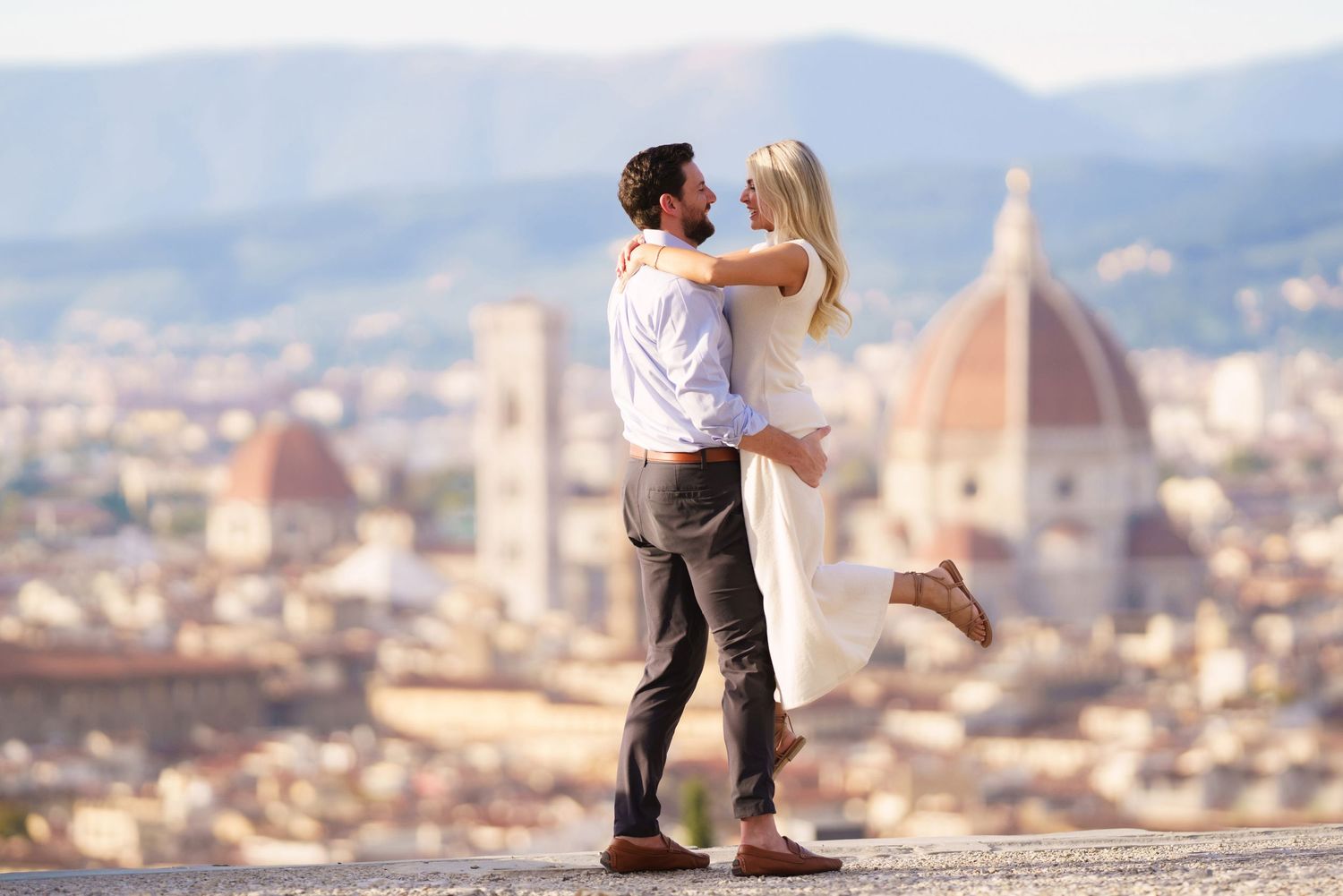 A couple shares a romantic moment overlooking the scenic cityscape of Florence, Italy with the Duomo cathedral visible.