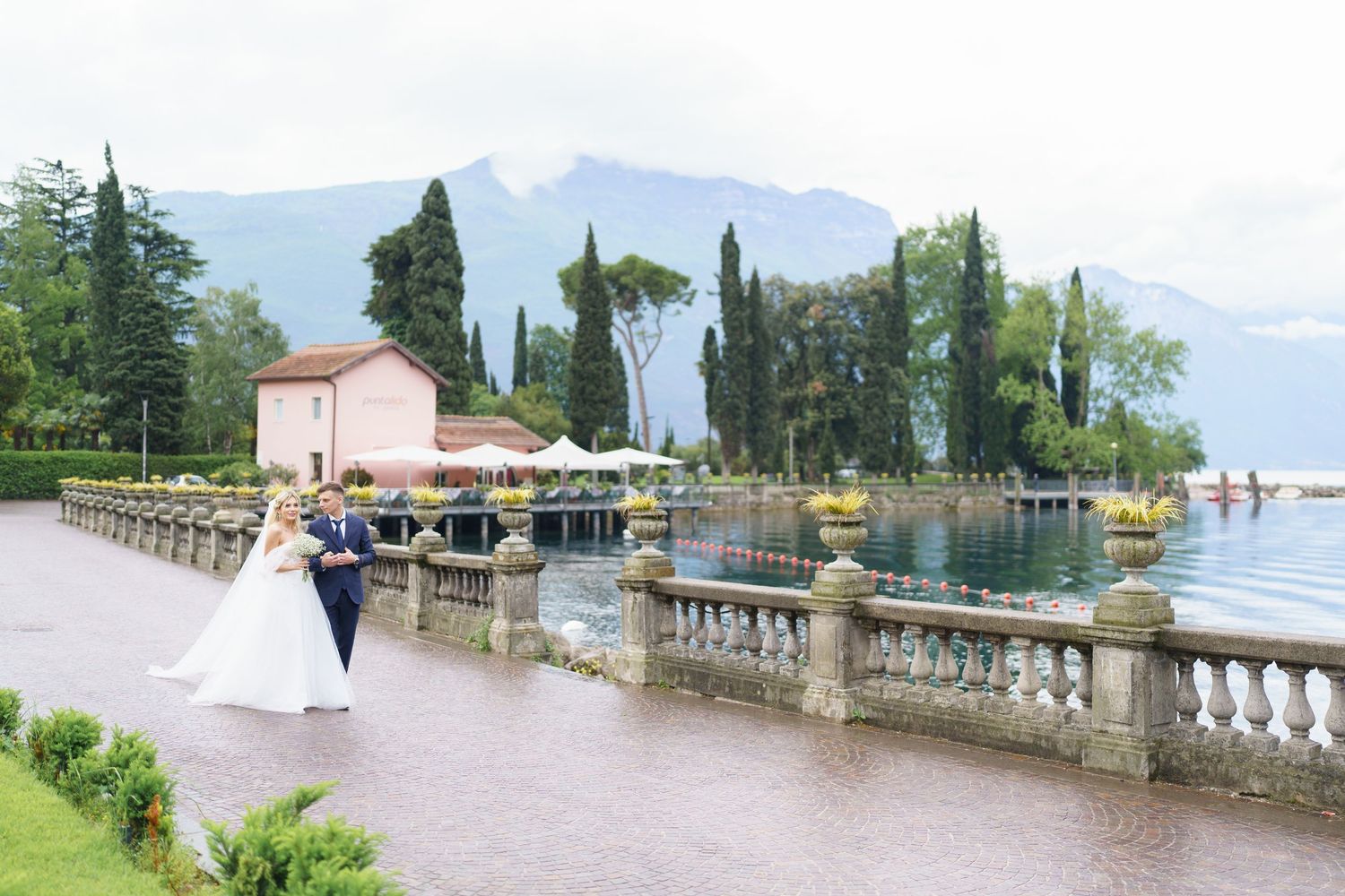 Scenic wedding couple photoshoot by Lake Como in Italy with mountains and elegant stone balustrades in the background.