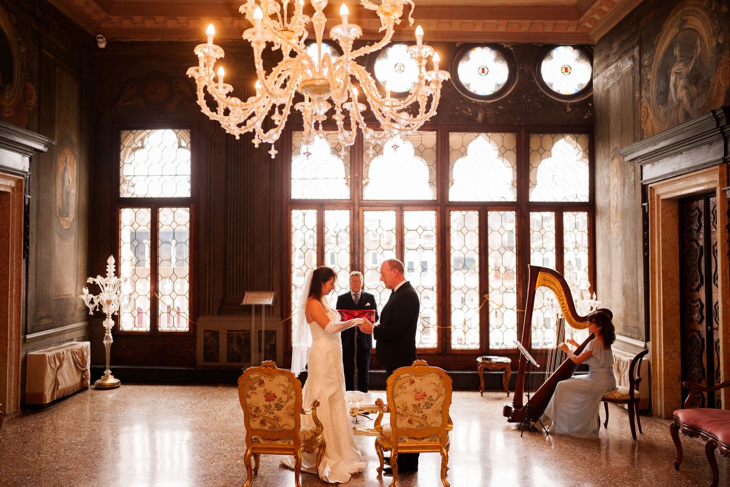 Elegant gothic-style room with ornate chandelier, arched windows, and antique furniture in warm wood tones.