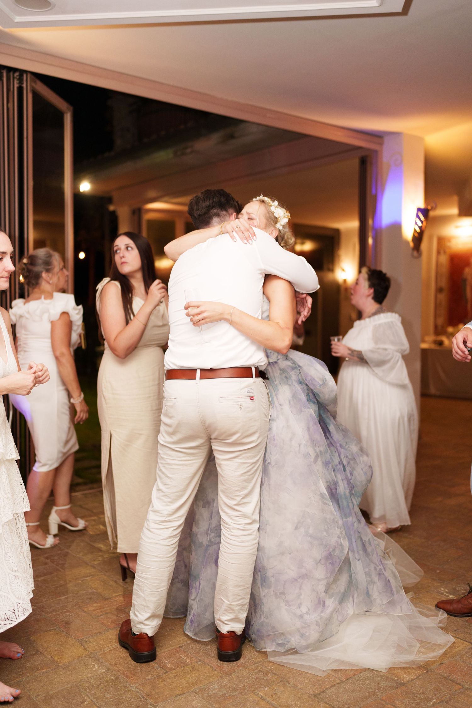 Bride and groom share a romantic first dance hug at their wedding reception, surrounded by guests in elegant attire.