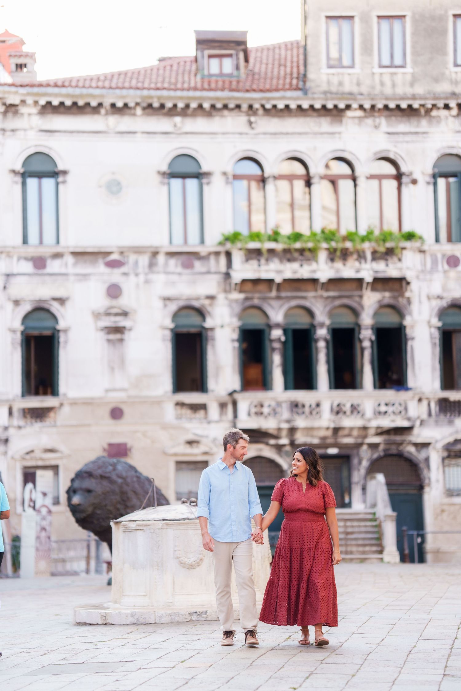 Couple holding hands walking in a Venetian square with historic architecture in Venice, Italy.