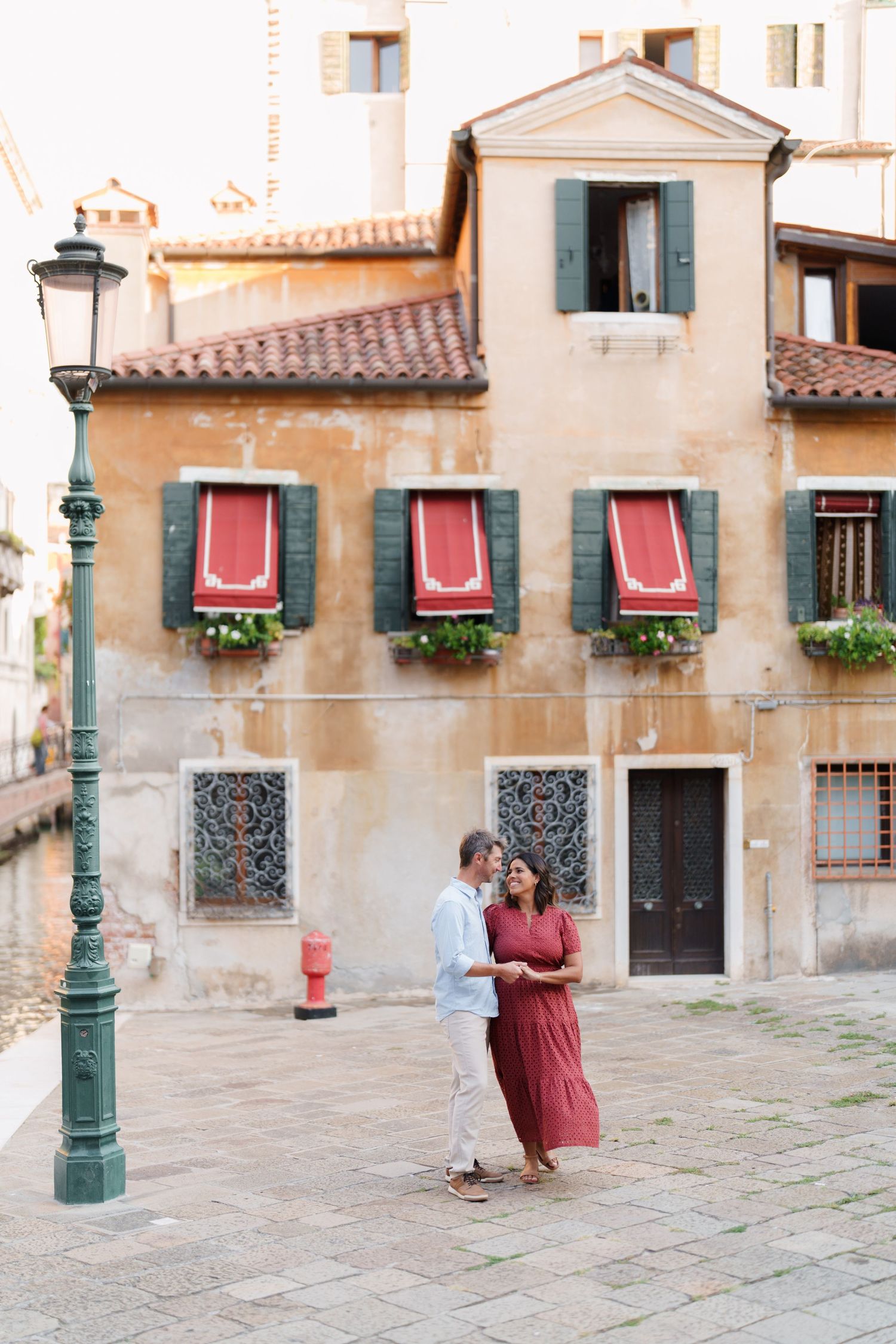 Romantic couple dancing on cobblestone street in Venice, Italy, with colorful shuttered building backdrop.