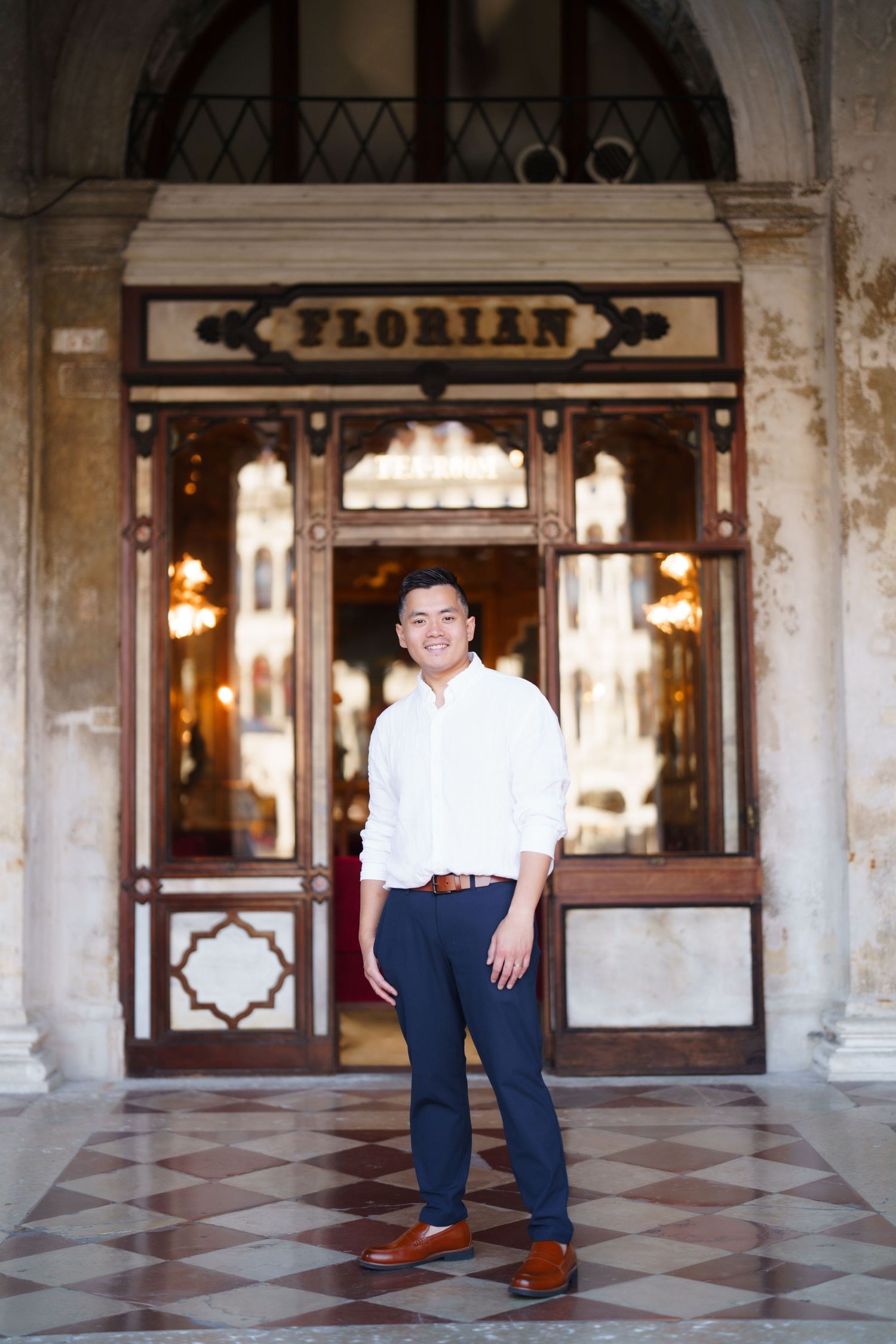 Man smiling in white shirt and navy pants standing in front of Caffe Florian in Venice, Italy.