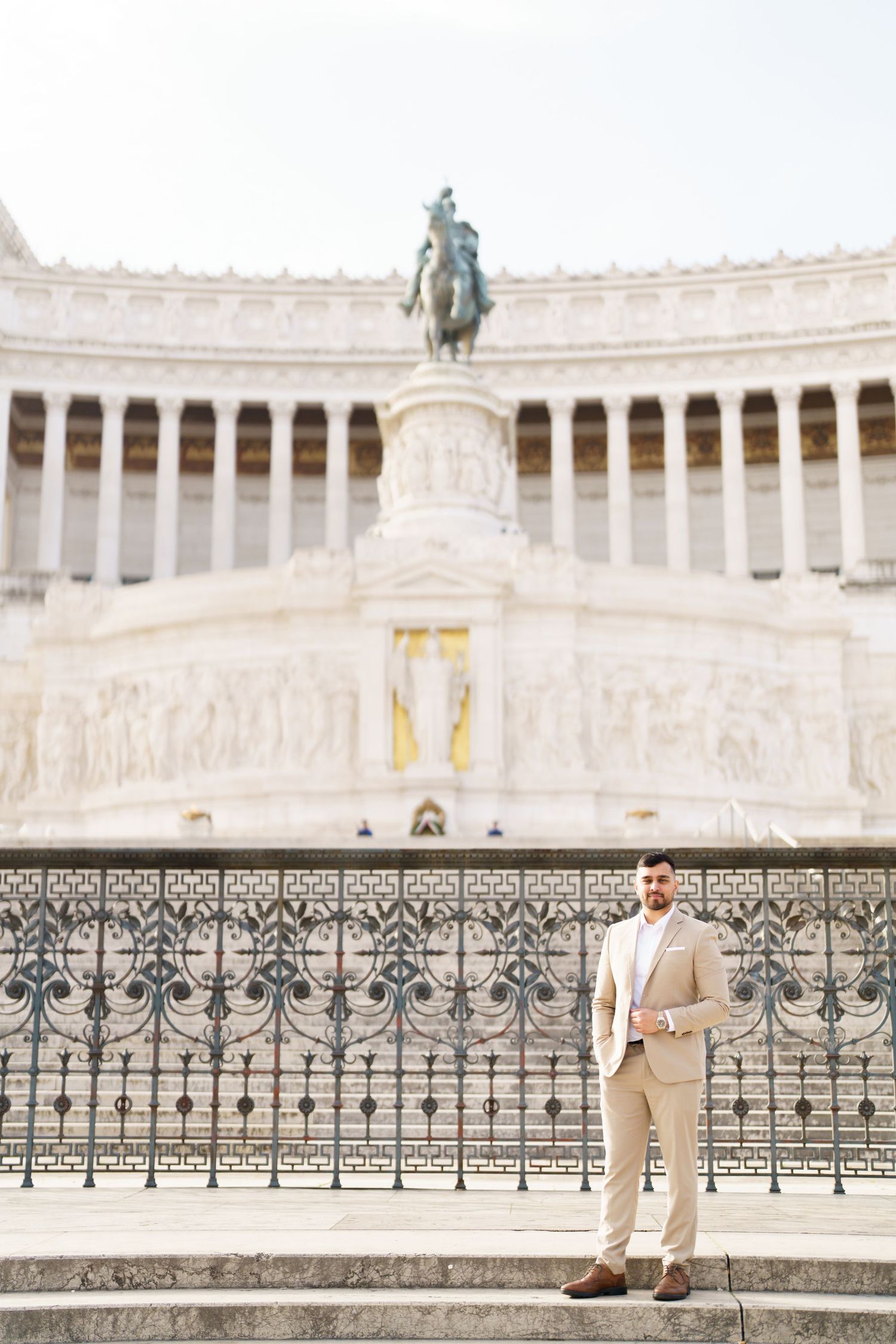 Man in beige suit standing before the Altare della Patria monument in Rome, Italy.