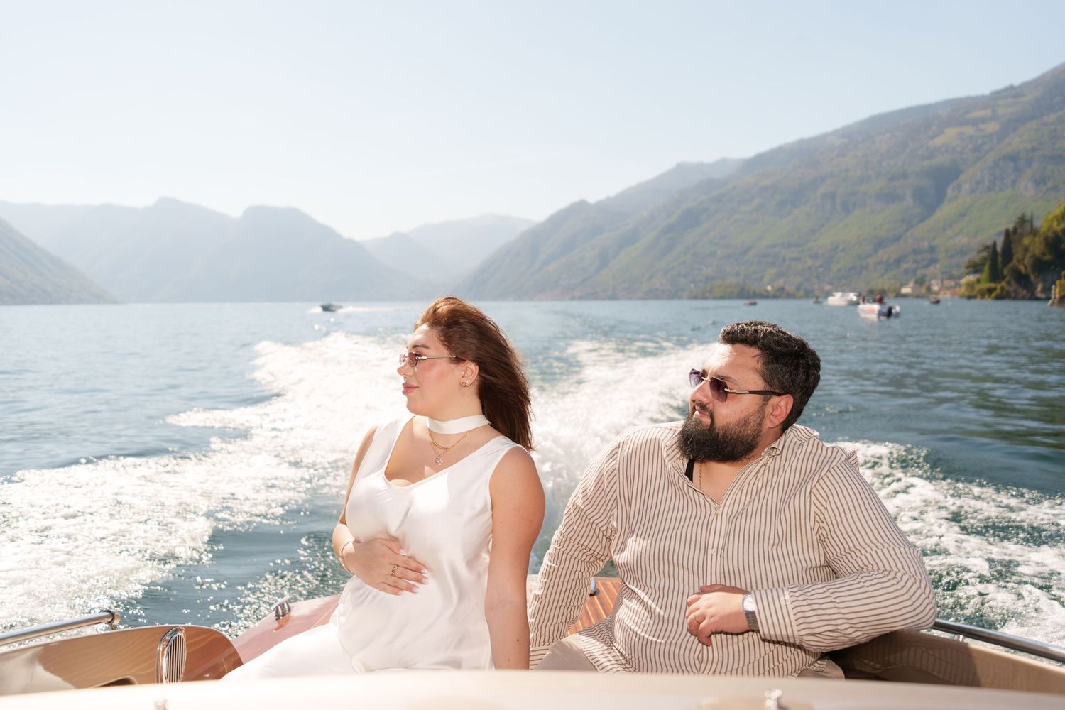 Couple relaxing on a luxury boat with stunning mountain lake views on a sunny day.