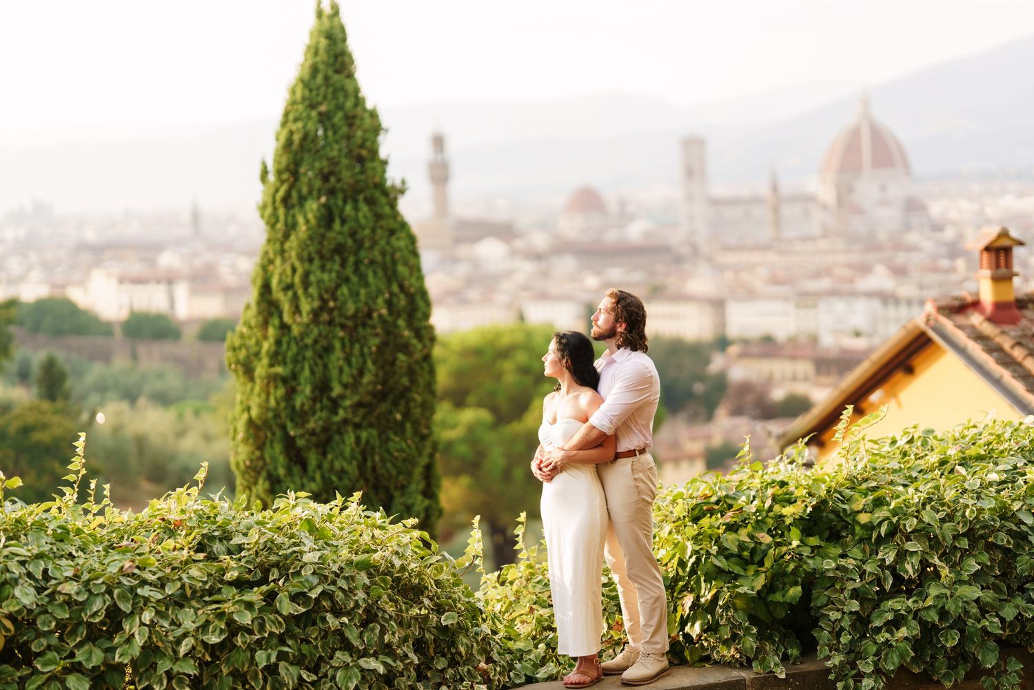 Couple embracing with Florence skyline, Duomo, and lush greenery in the background at golden hour.