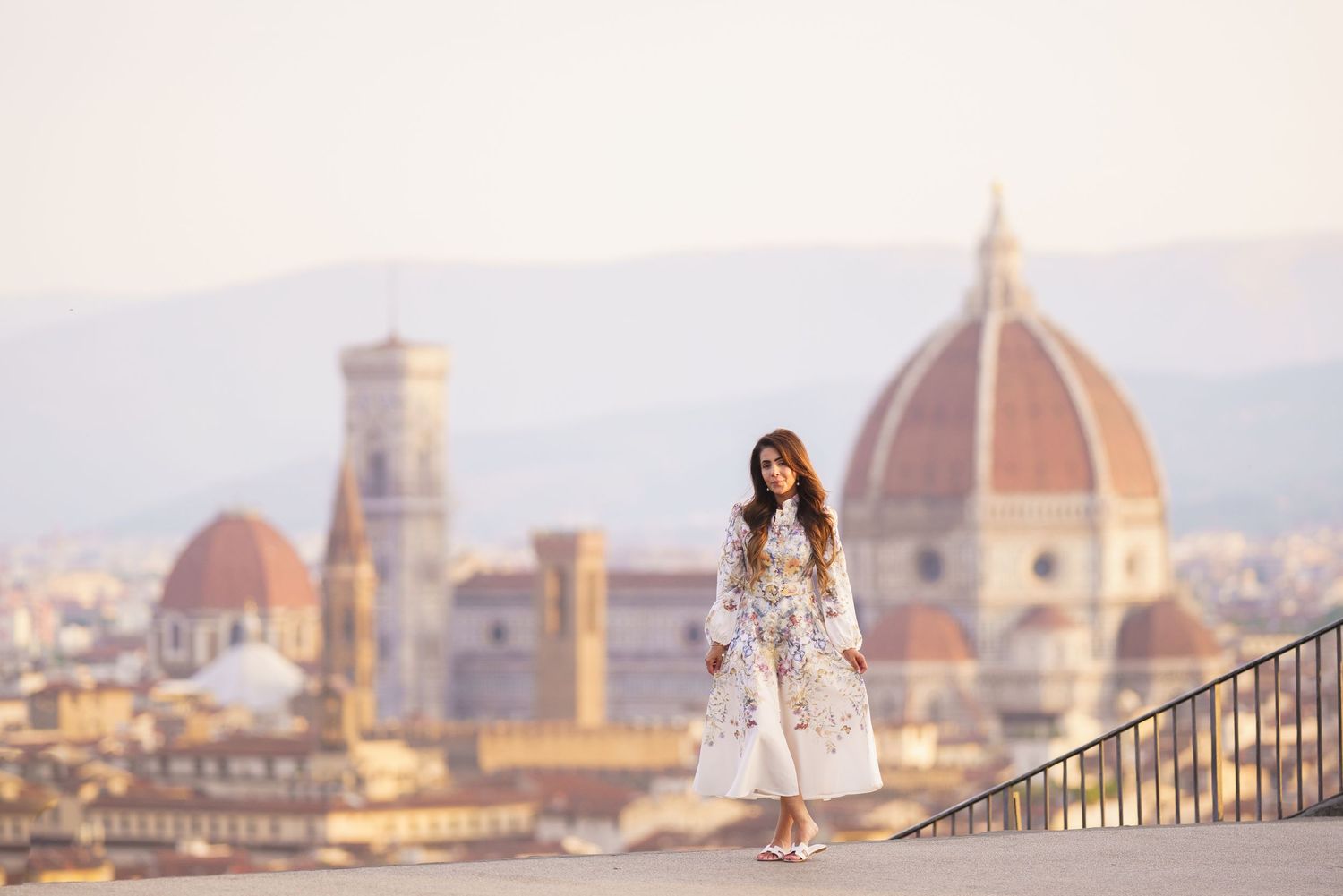 Woman in floral dress poses on rooftop terrace with Florence Cathedral dome and cityscape in golden light.
