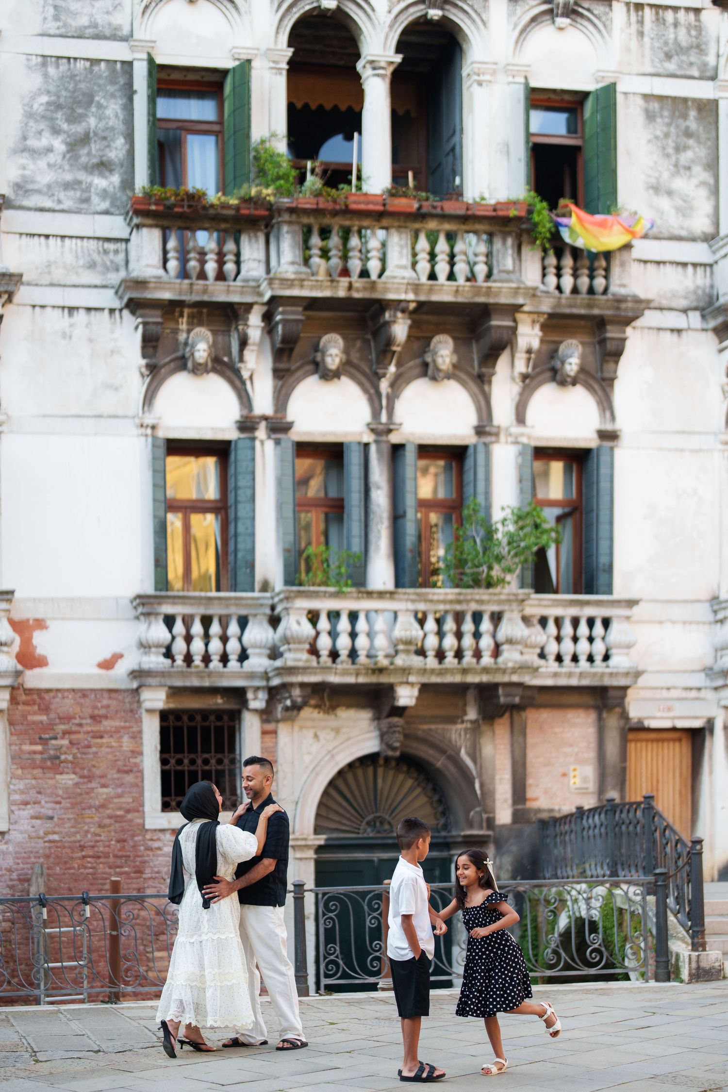 Family of four enjoying a sunny day in Venice, Italy, with ornate historic building facade in background.