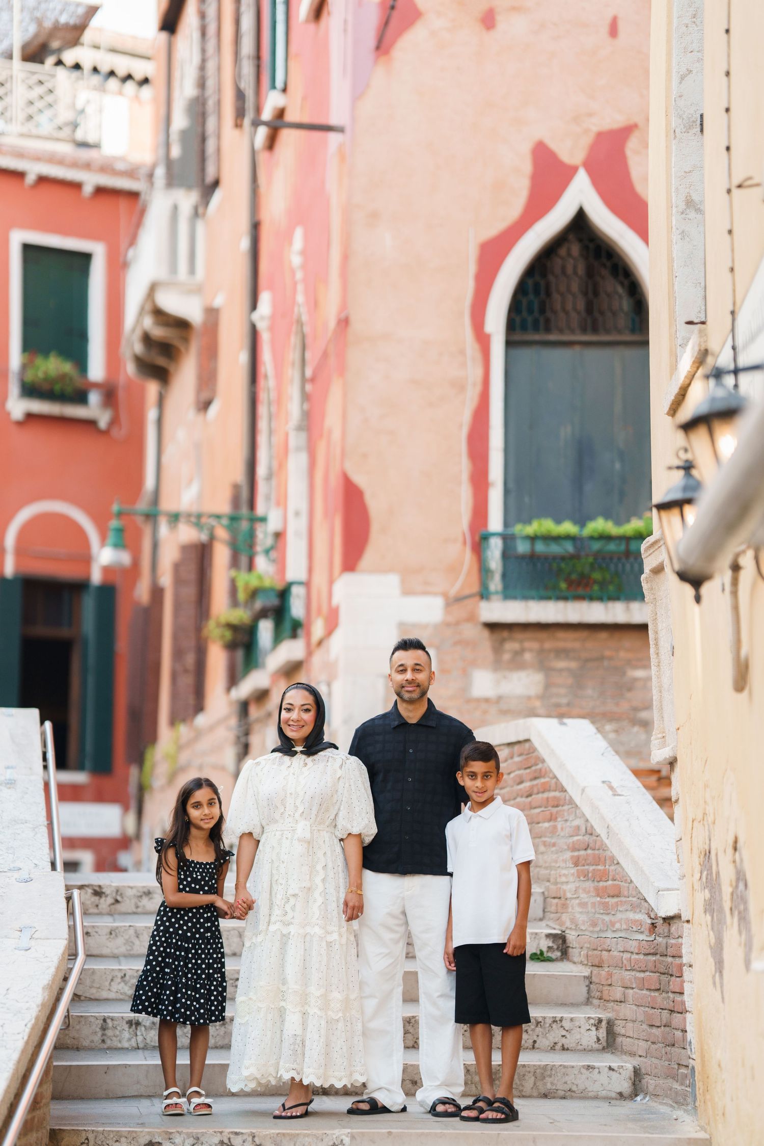 Family of four posing on stone steps in Venice, Italy, with colorful historic buildings in the background.