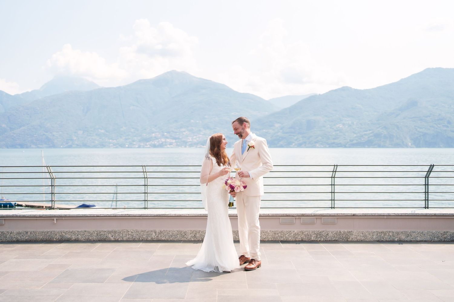 Bride and groom stand together on a lakeside terrace with mountain views on their wedding day.