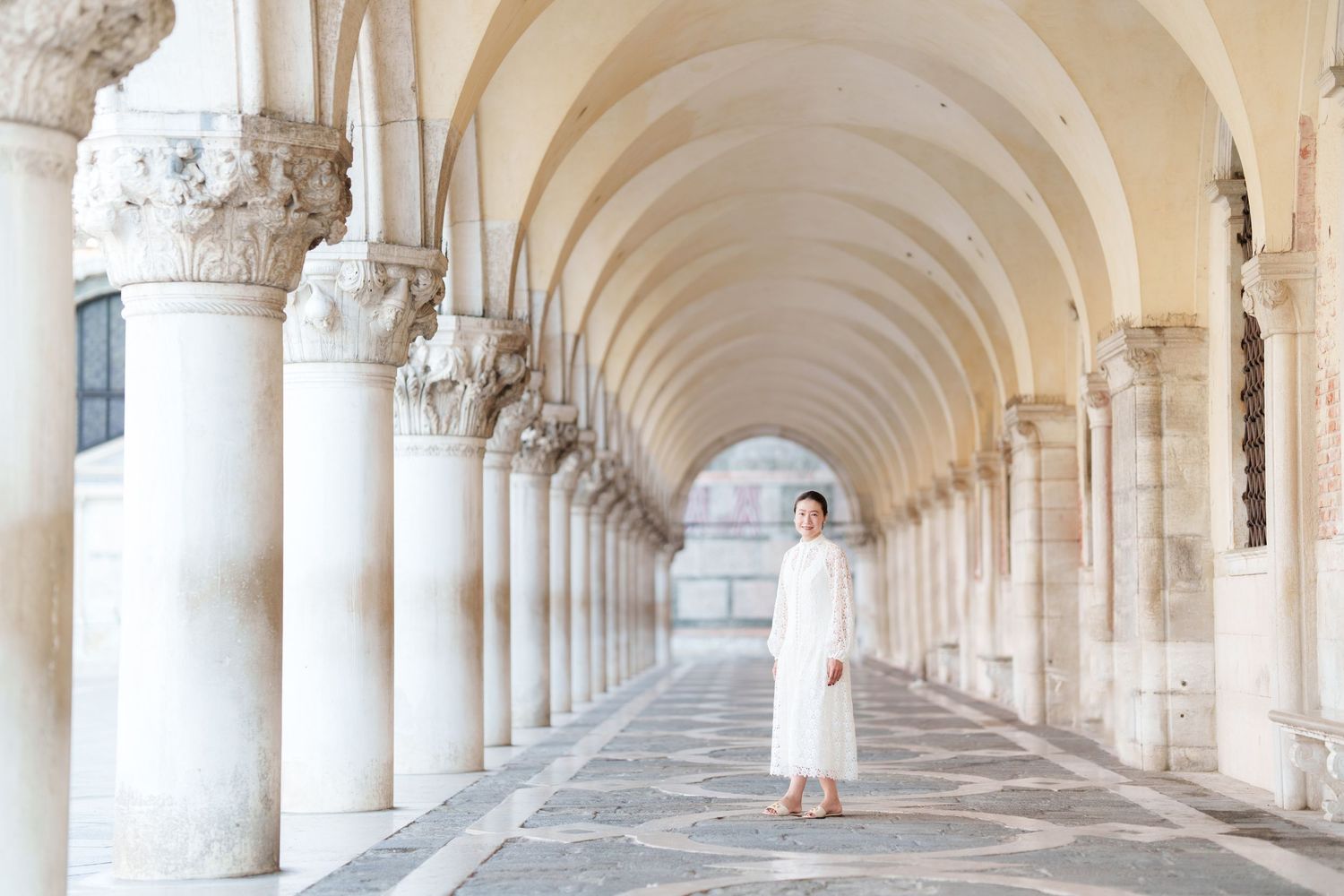 Woman in white dress standing under elegant arched colonnade in Venice, Italy.