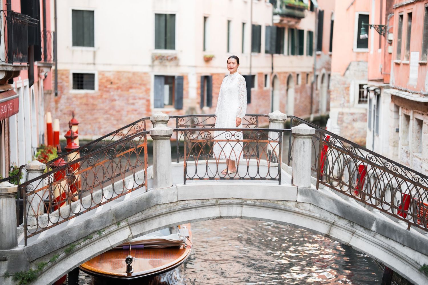 Woman in white dress standing on a charming Venice canal bridge with boats and historic buildings.