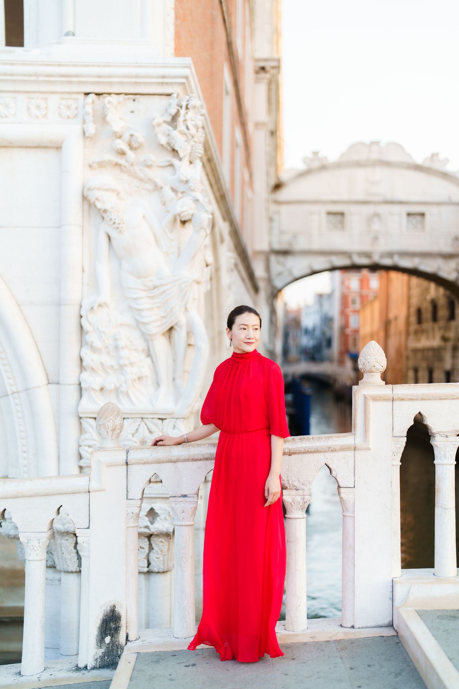 Woman in red dress poses near Bridge of Sighs in Venice, Italy.