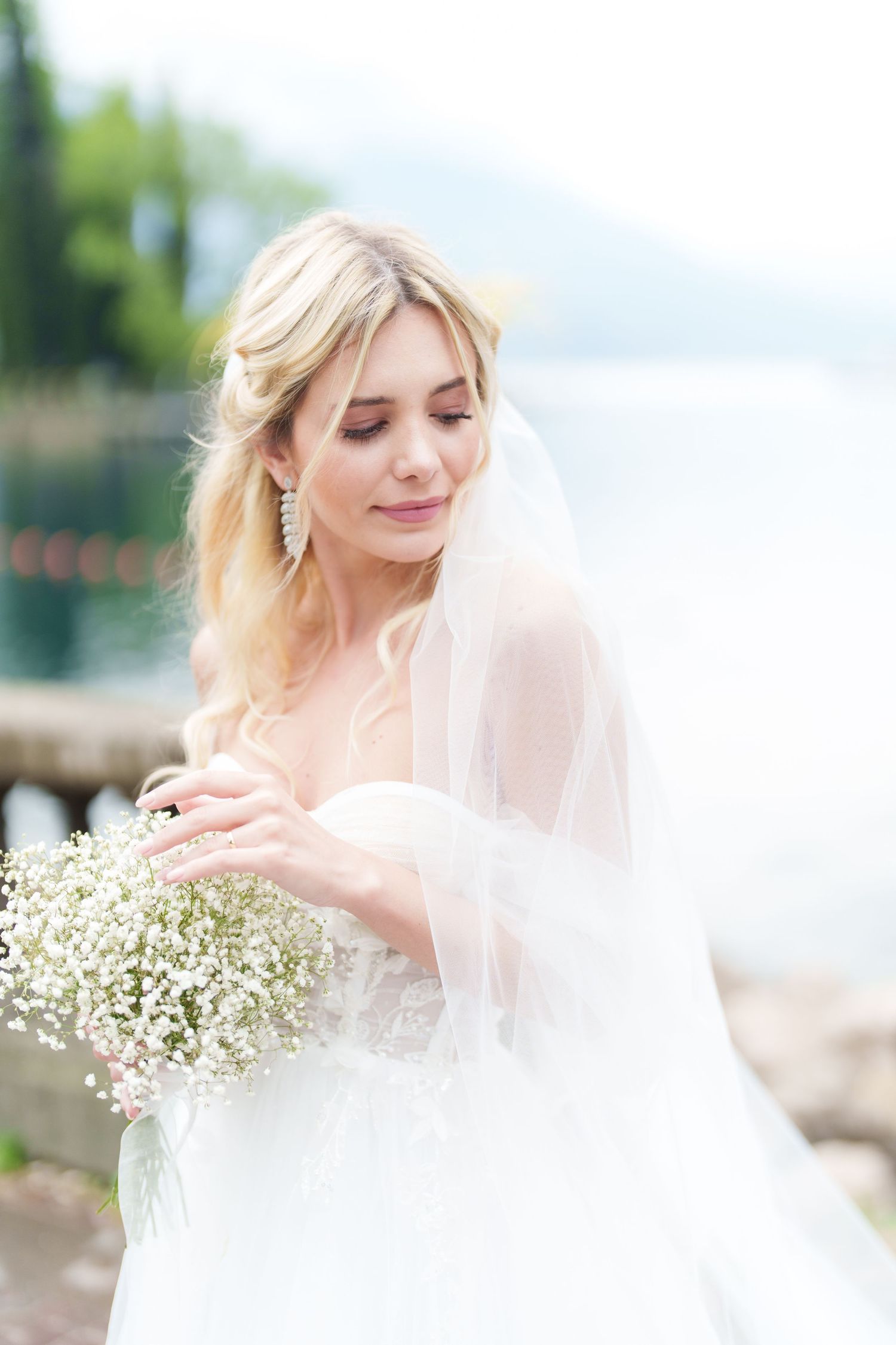 A bride in a white dress and veil holds delicate baby's breath flowers in an outdoor setting.