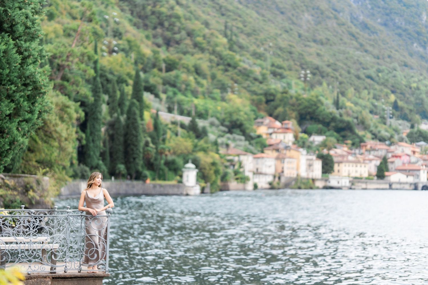 People enjoying a scenic lakeside promenade with mountains and buildings along Lake Como in Italy.