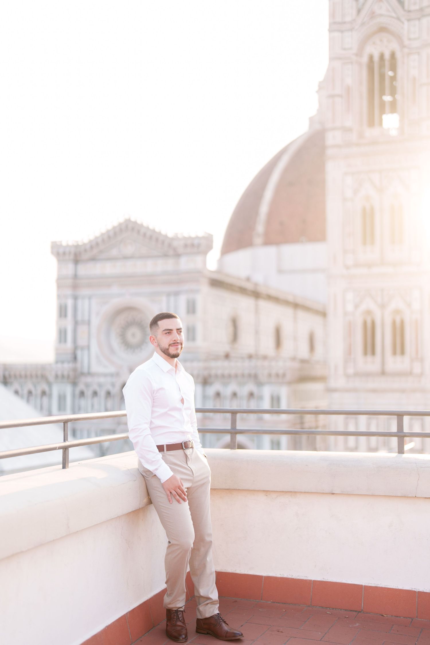 Person in white shirt and khaki pants stands on rooftop terrace with cathedral architecture in background at sunset.