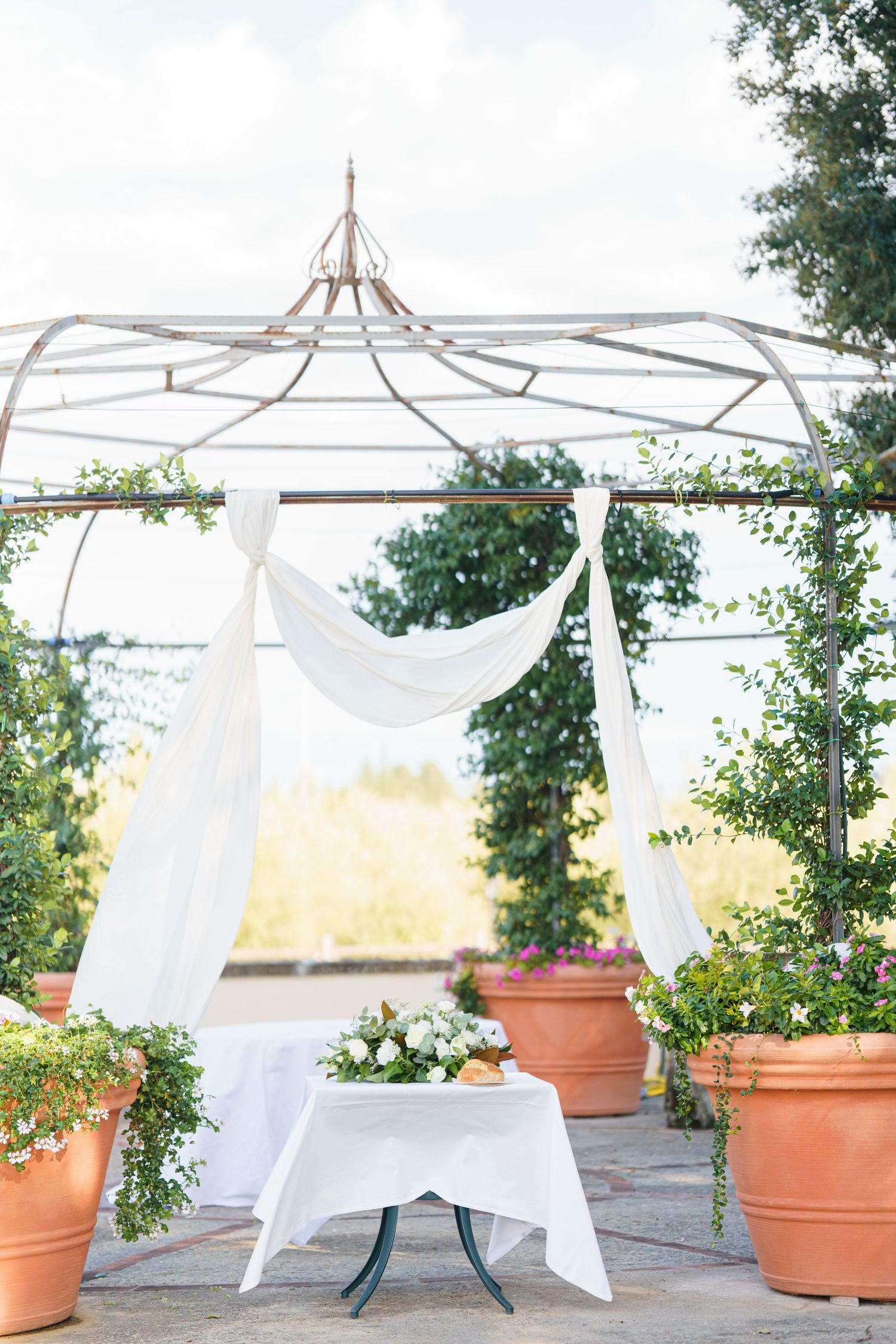 Flowing white curtains and terracotta pots decorate an outdoor pergola space.