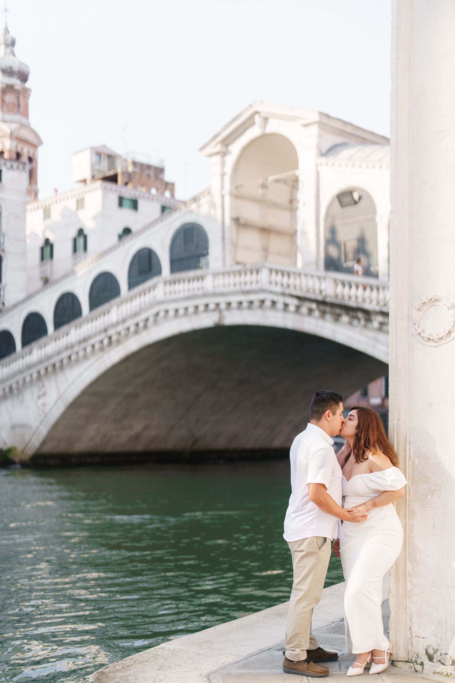 Romantic couple sharing intimate moments by the Rialto Bridge in Venice along the Grand Canal's turquoise waters.
