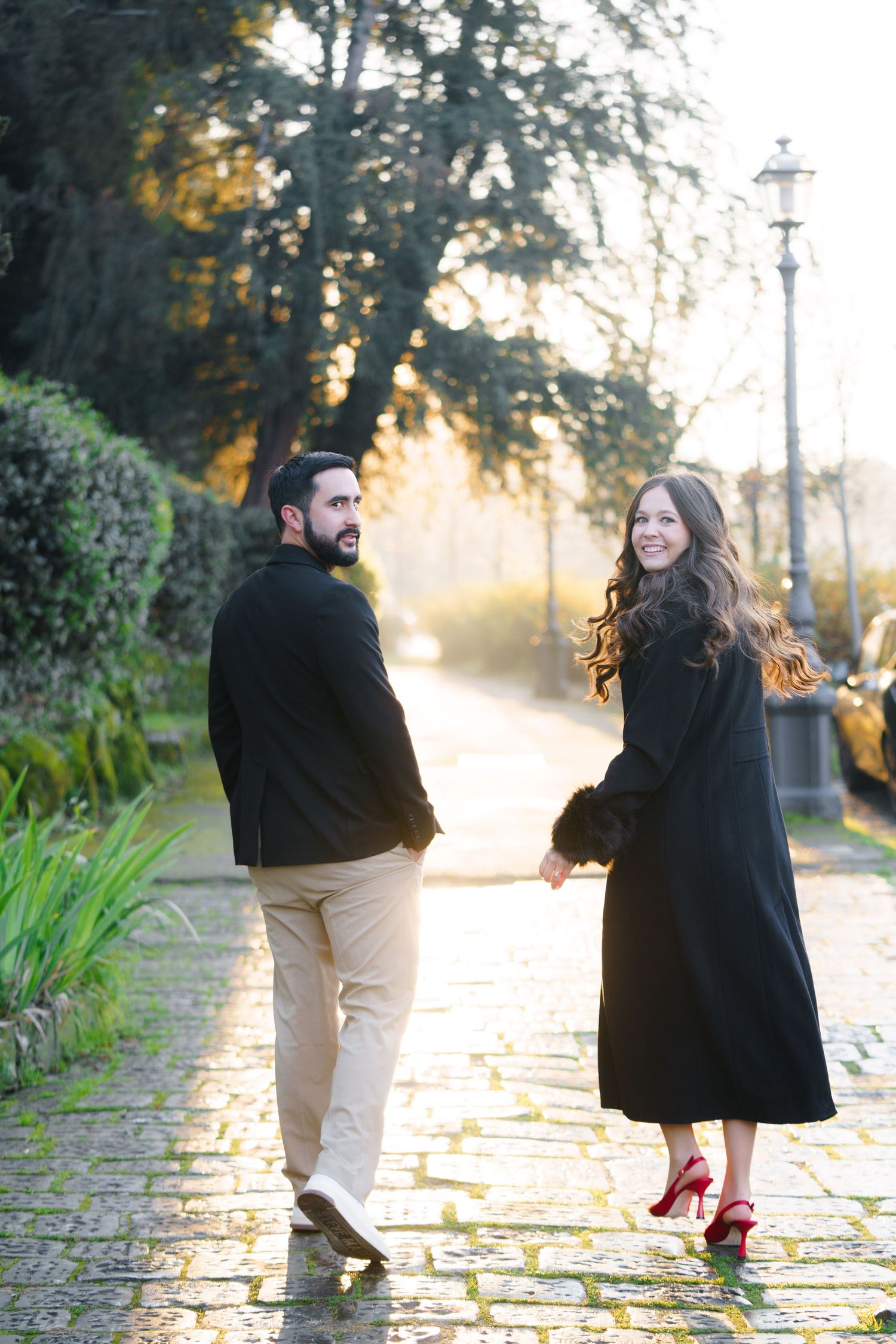 A couple walks along a cobblestone path during golden hour, creating a romantic autumn scene.