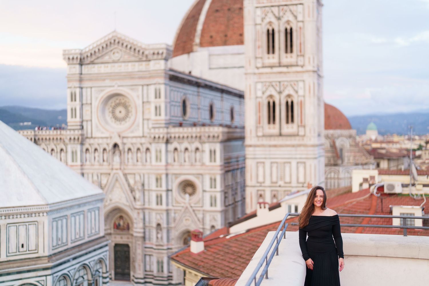View of Florence Cathedral's iconic dome and facade with terracotta rooftops in the foreground during sunset.
