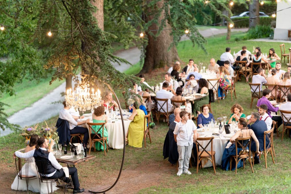 Elegant outdoor wedding celebration with guests seated at tables among trees.
