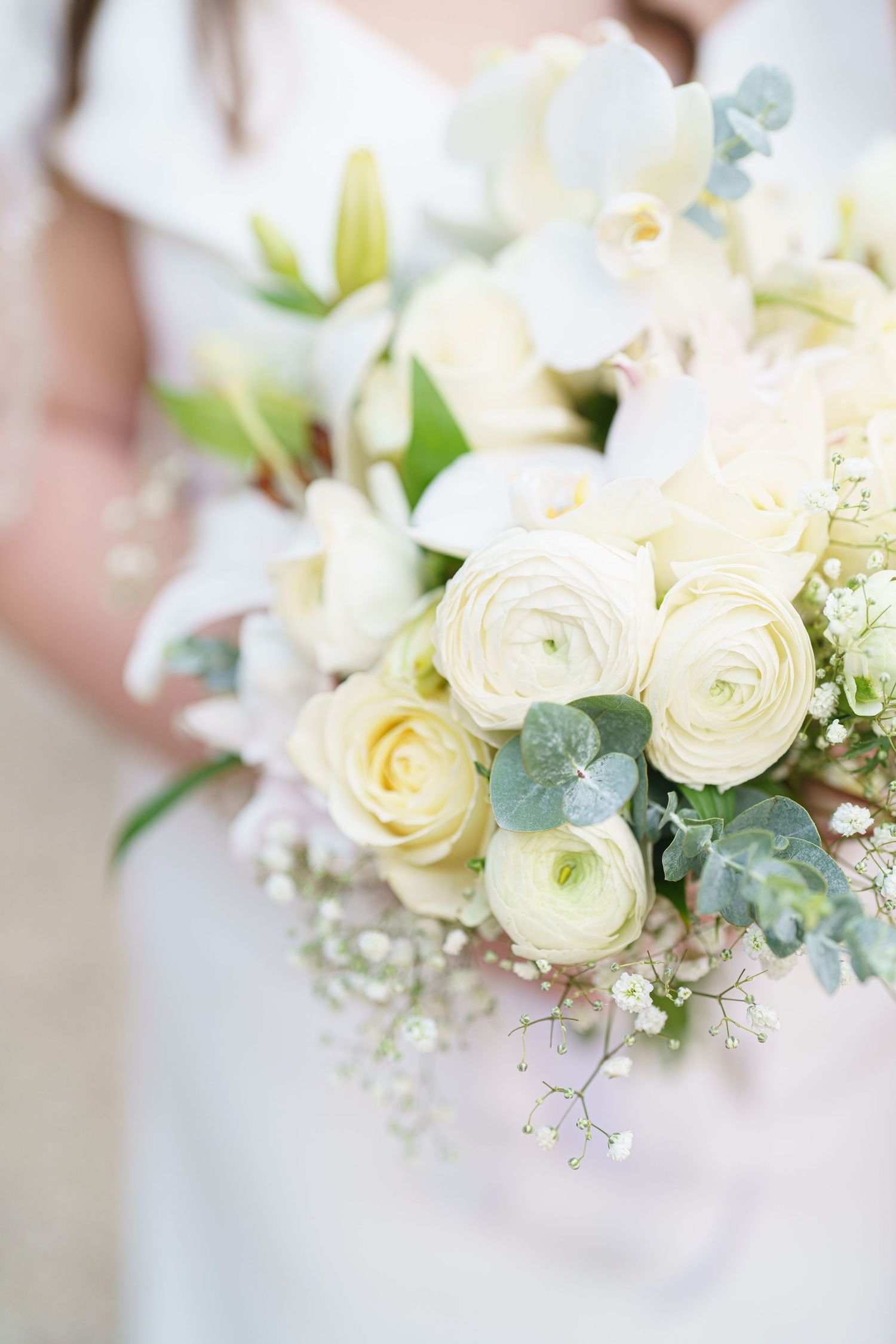 Elegant white ranunculus and eucalyptus wedding bouquet with delicate details.