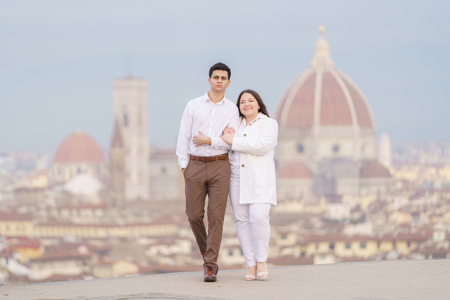 Couple in coordinated white and brown outfits walking with Florence's Duomo cathedral behind them.