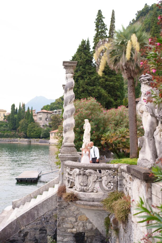 Historic villa terrace with ornate stone columns and statues along Lake Como's waterfront.