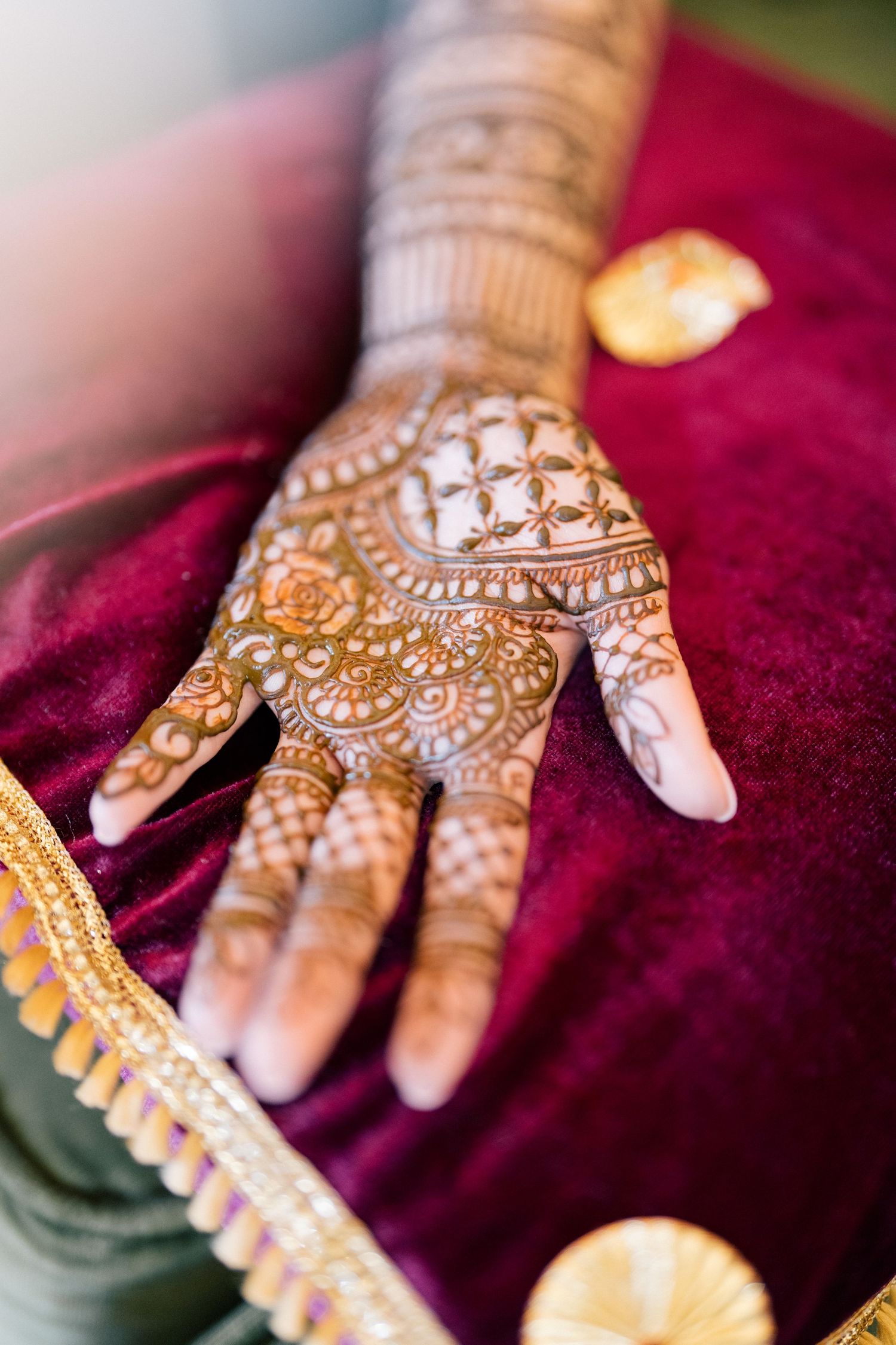 Intricate henna designs adorning hands displayed on rich burgundy fabric.