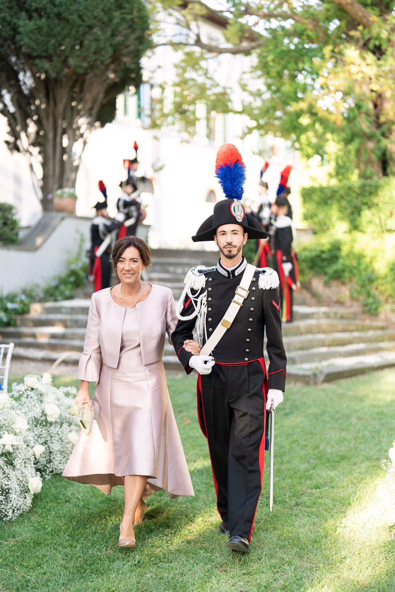 Military officers in ceremonial uniforms walking down garden steps.