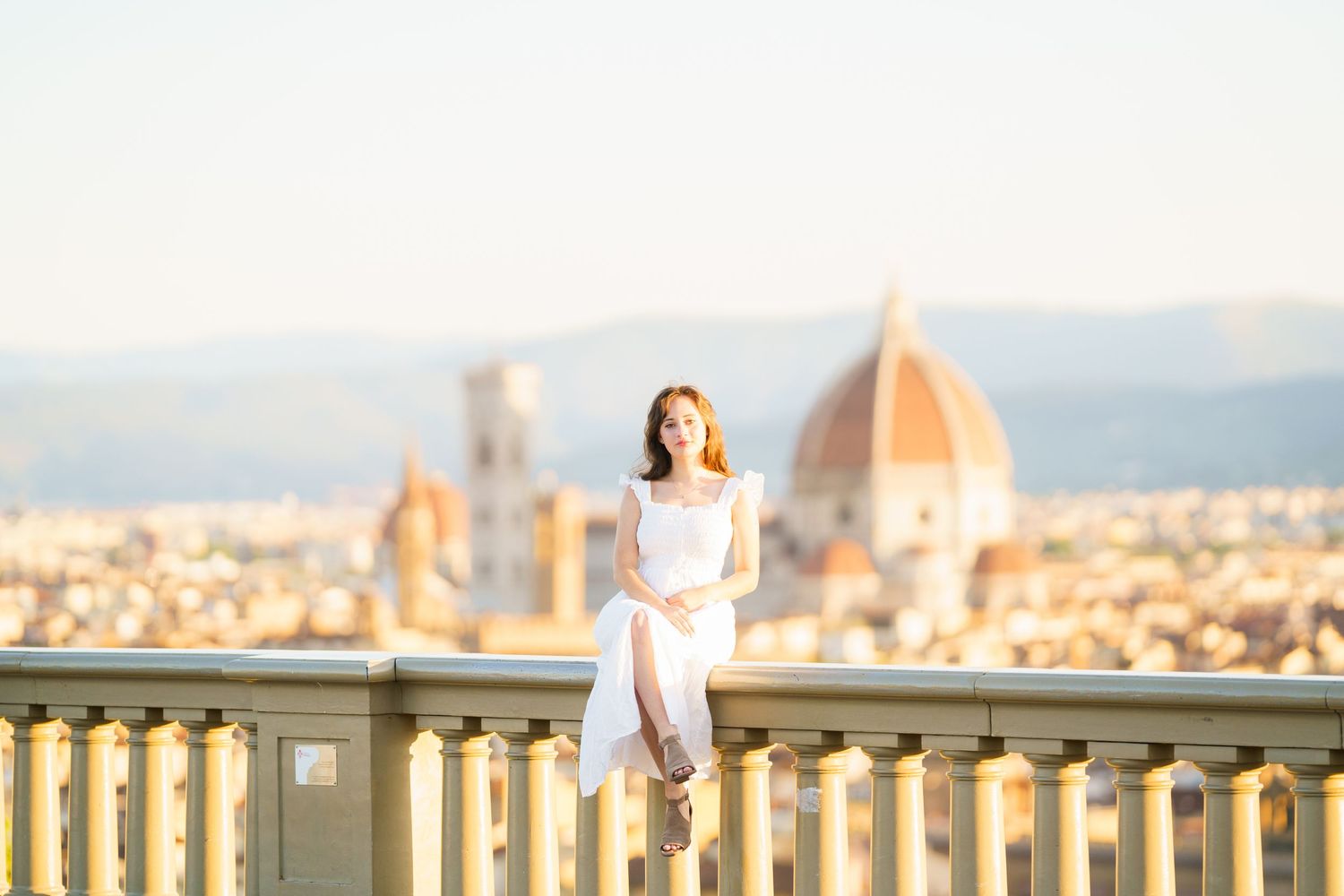 A person in a white dress admires the stunning panoramic view of Florence, Italy with the Duomo cathedral in the distance.