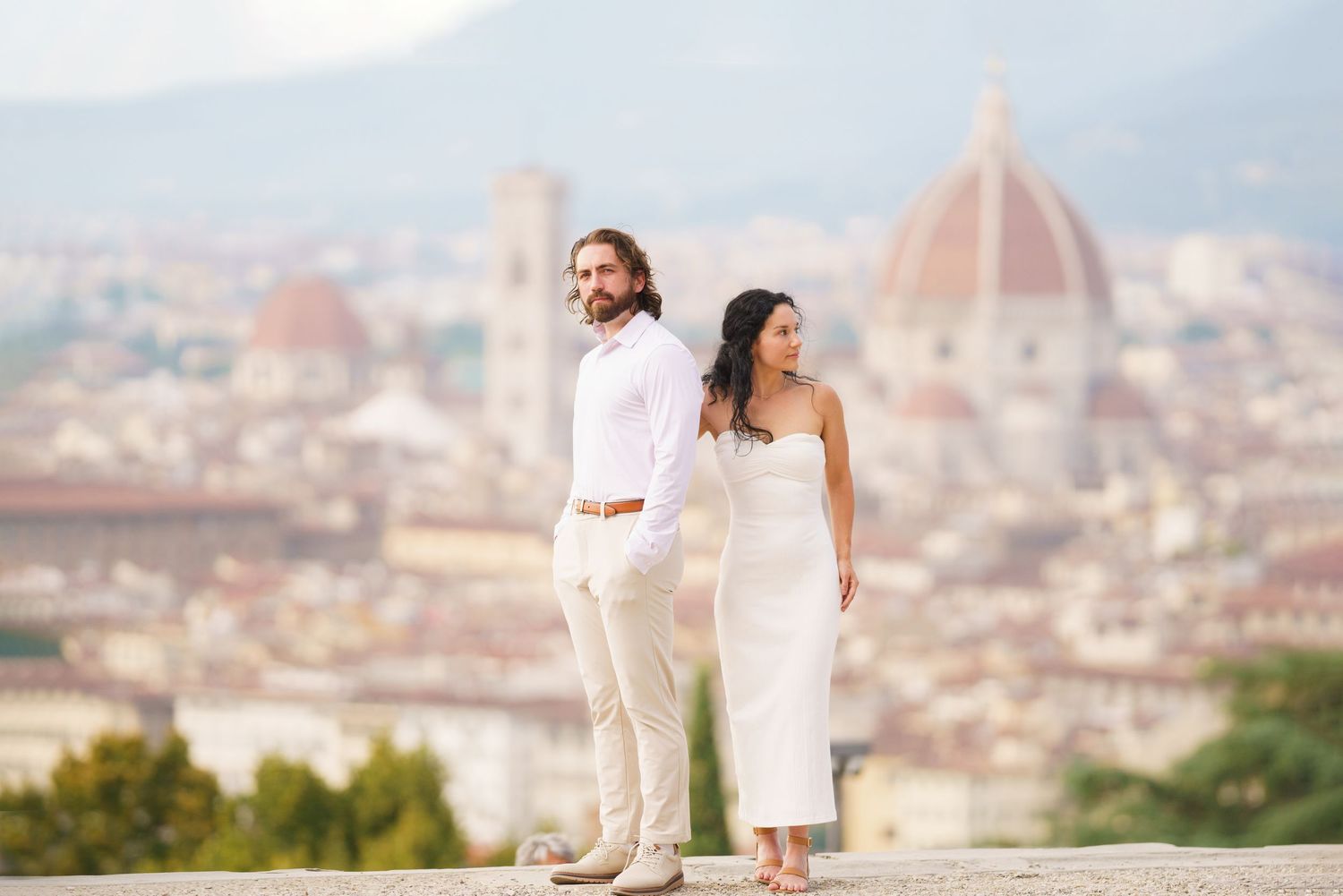Romantic couple in white outfits poses against scenic Florence cityscape with Duomo cathedral in background.