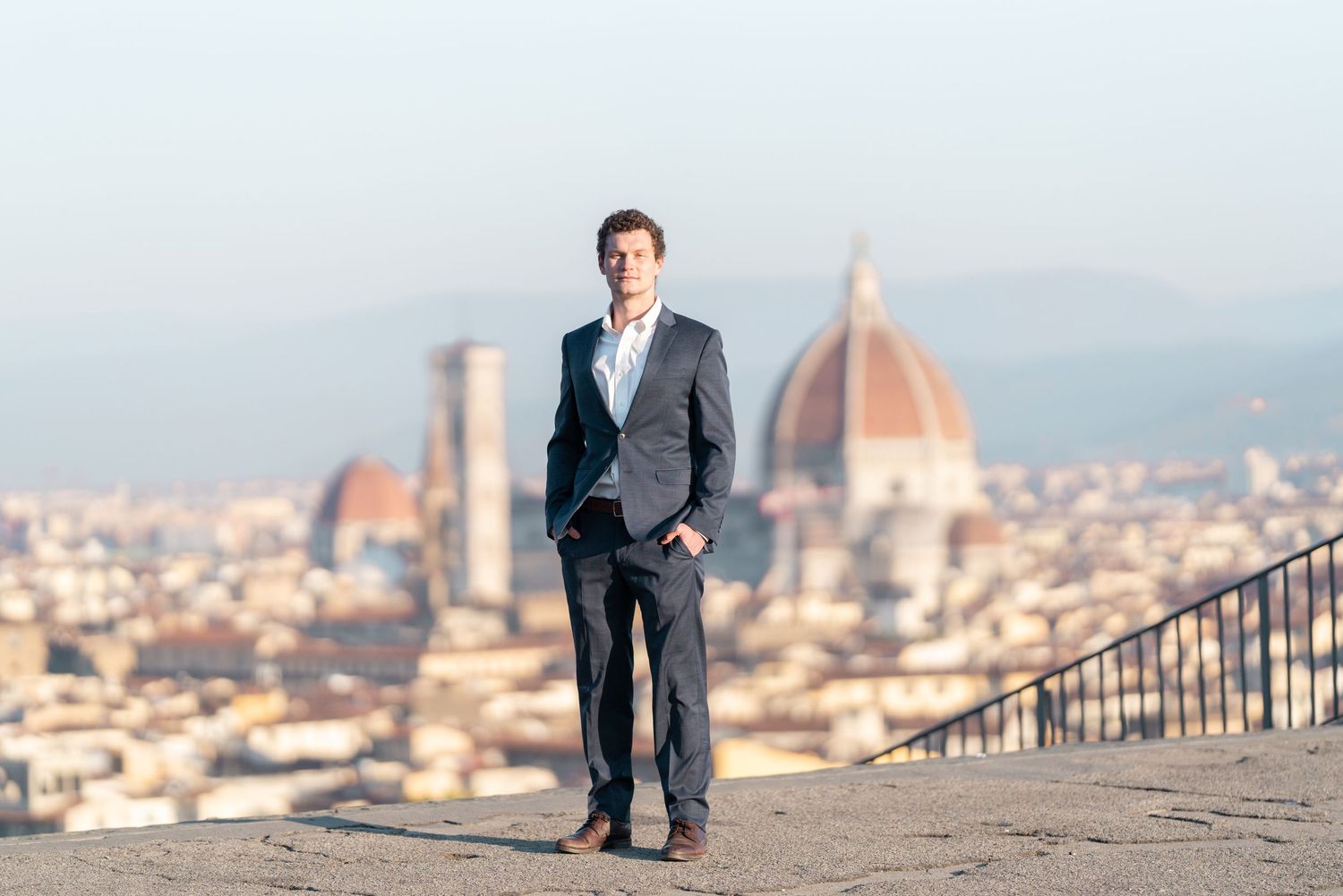 Person in a suit poses on a scenic overlook with the iconic Duomo cathedral dome and Florence cityscape in the background.