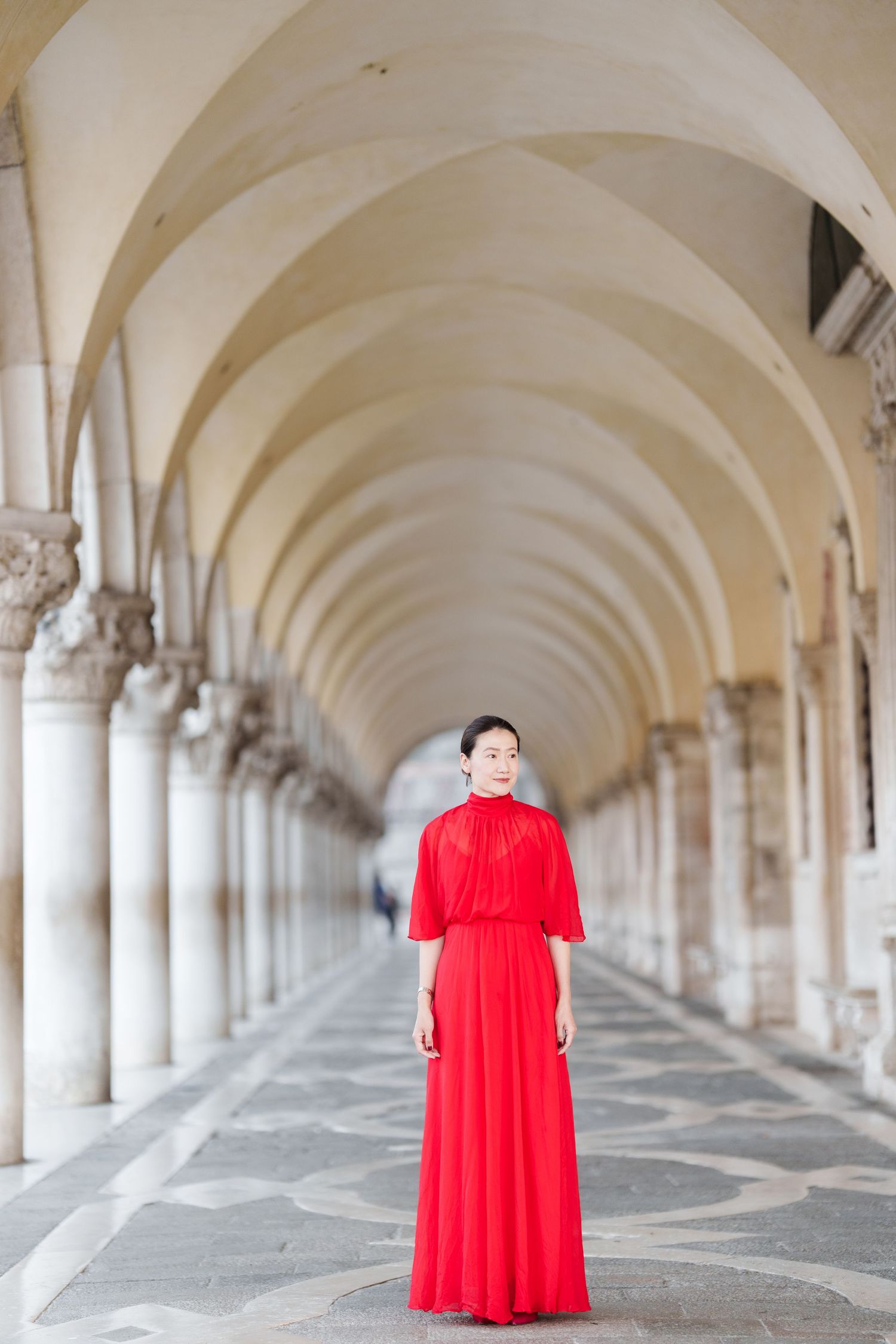 Woman in elegant red gown standing in arched colonnade of Doge's Palace, Venice, Italy.