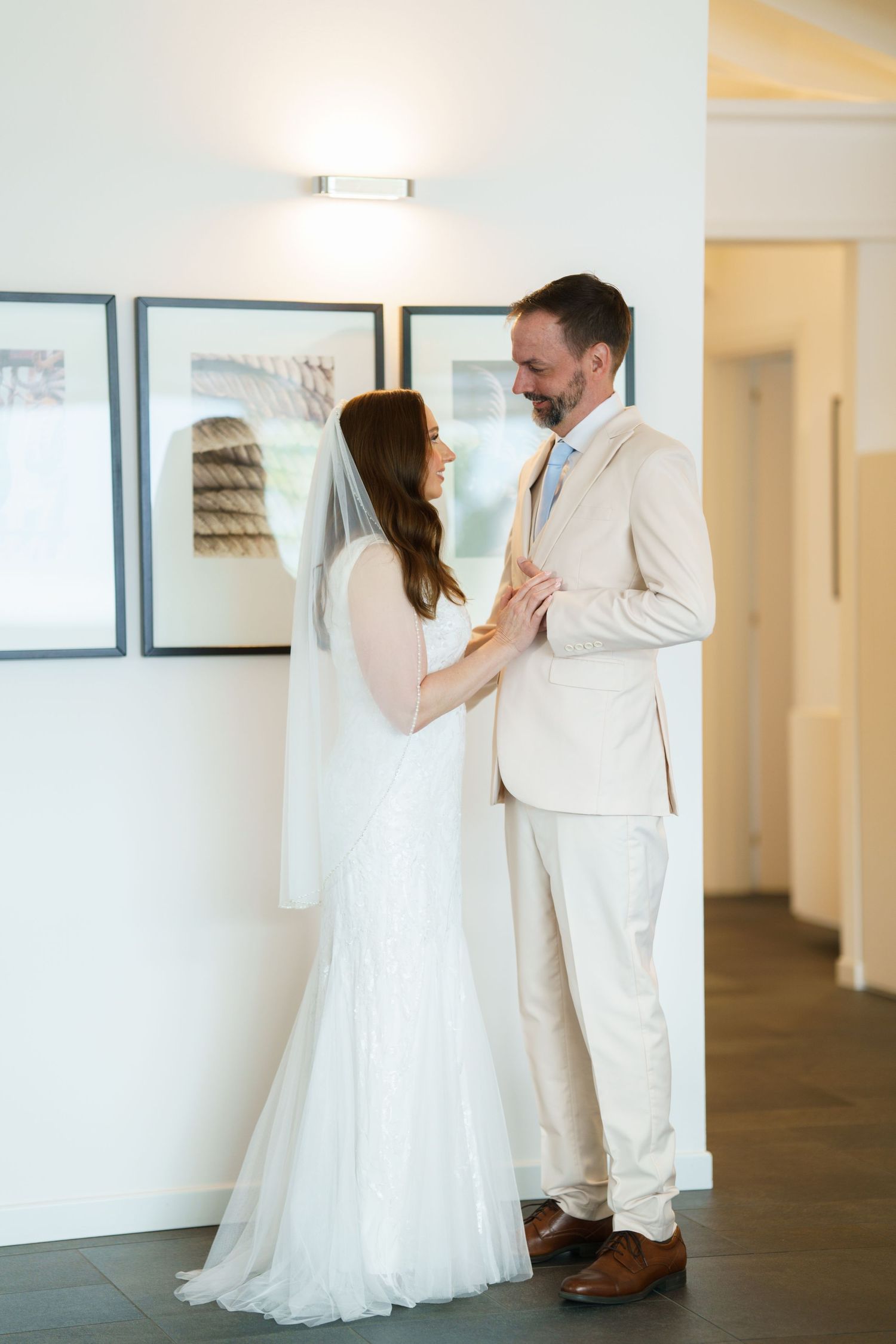 Bride and groom share a tender moment in elegant wedding attire, standing together in a bright, modern interior.
