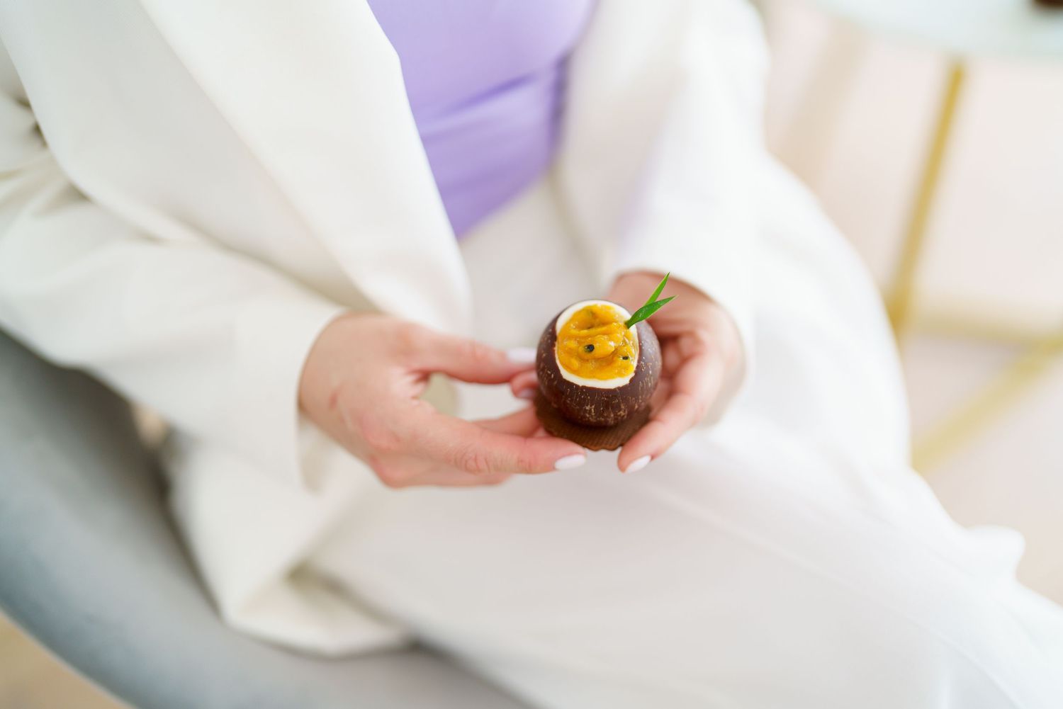 Person in white outfit holding a chocolate tart topped with passion fruit and a mint leaf.