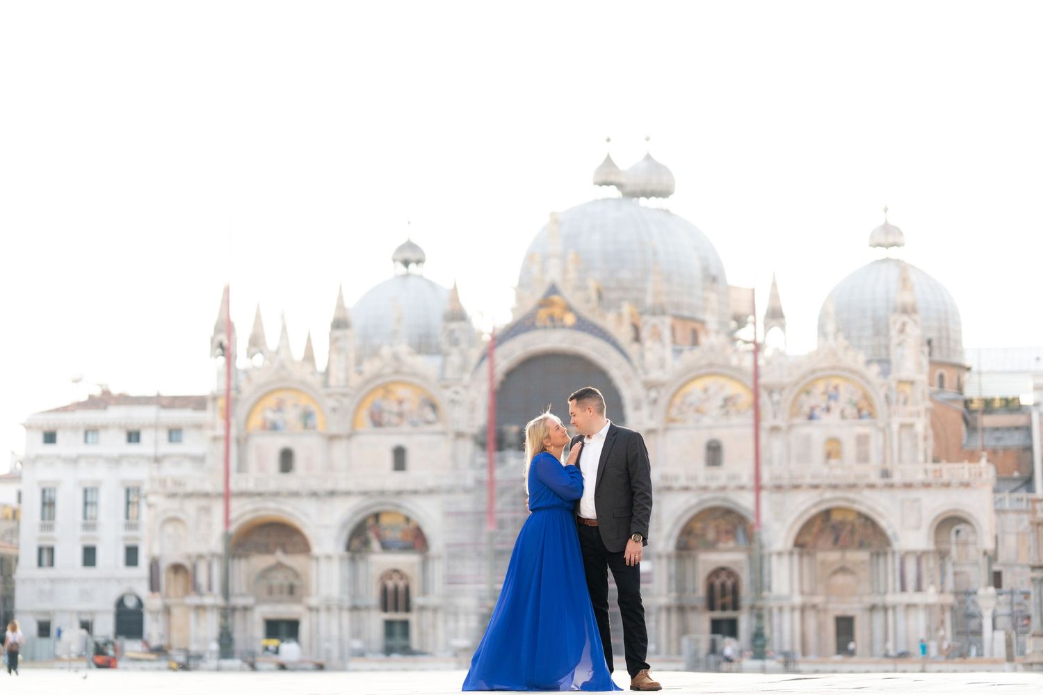 Couple in formal attire poses in front of St. Mark's Basilica in Venice during golden hour.