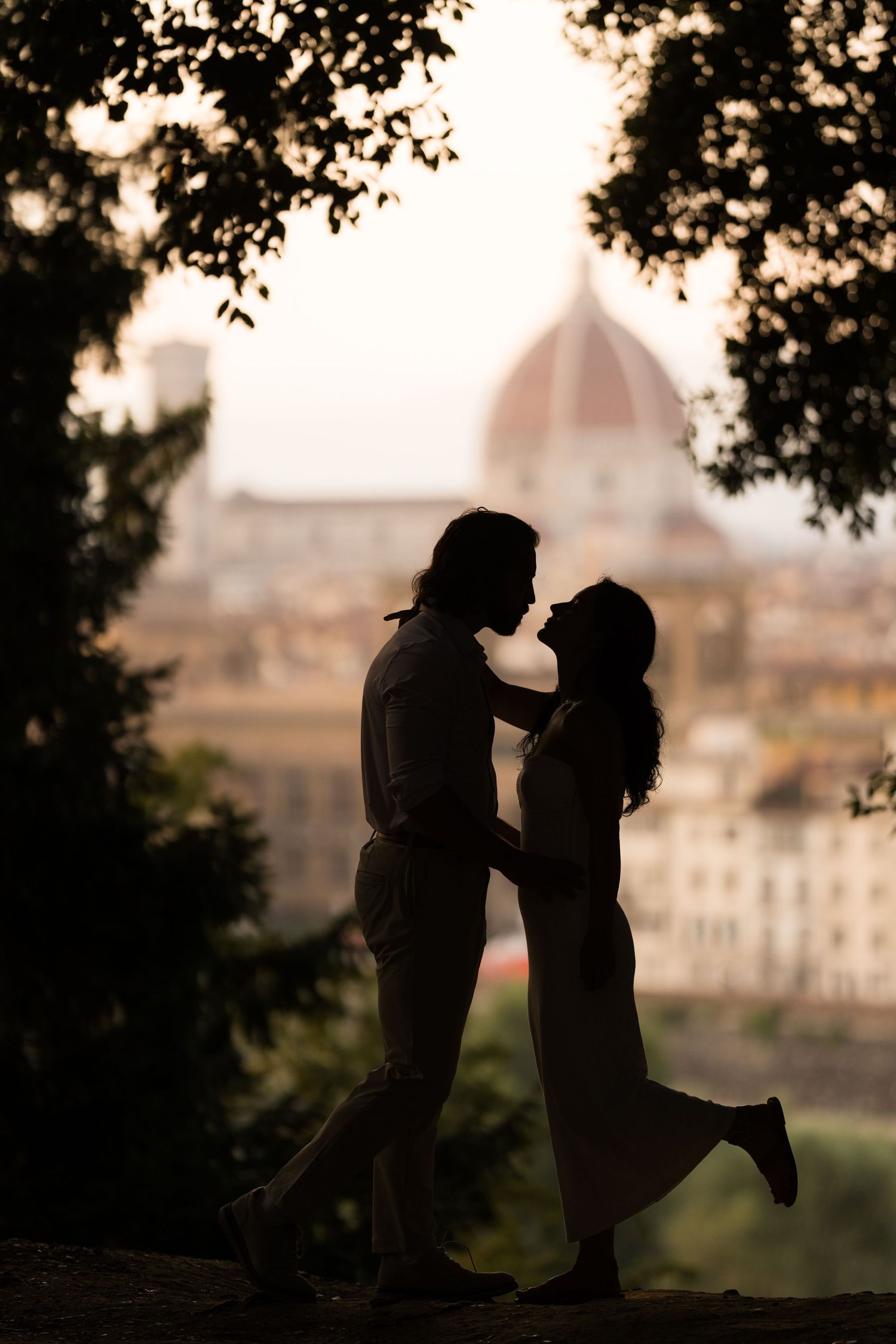 Romantic silhouette of a couple embracing at sunset with Florence's Duomo cathedral dome visible in the background.